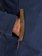 Close-up of a navy blue jacket with a brown leather strap and zipper.