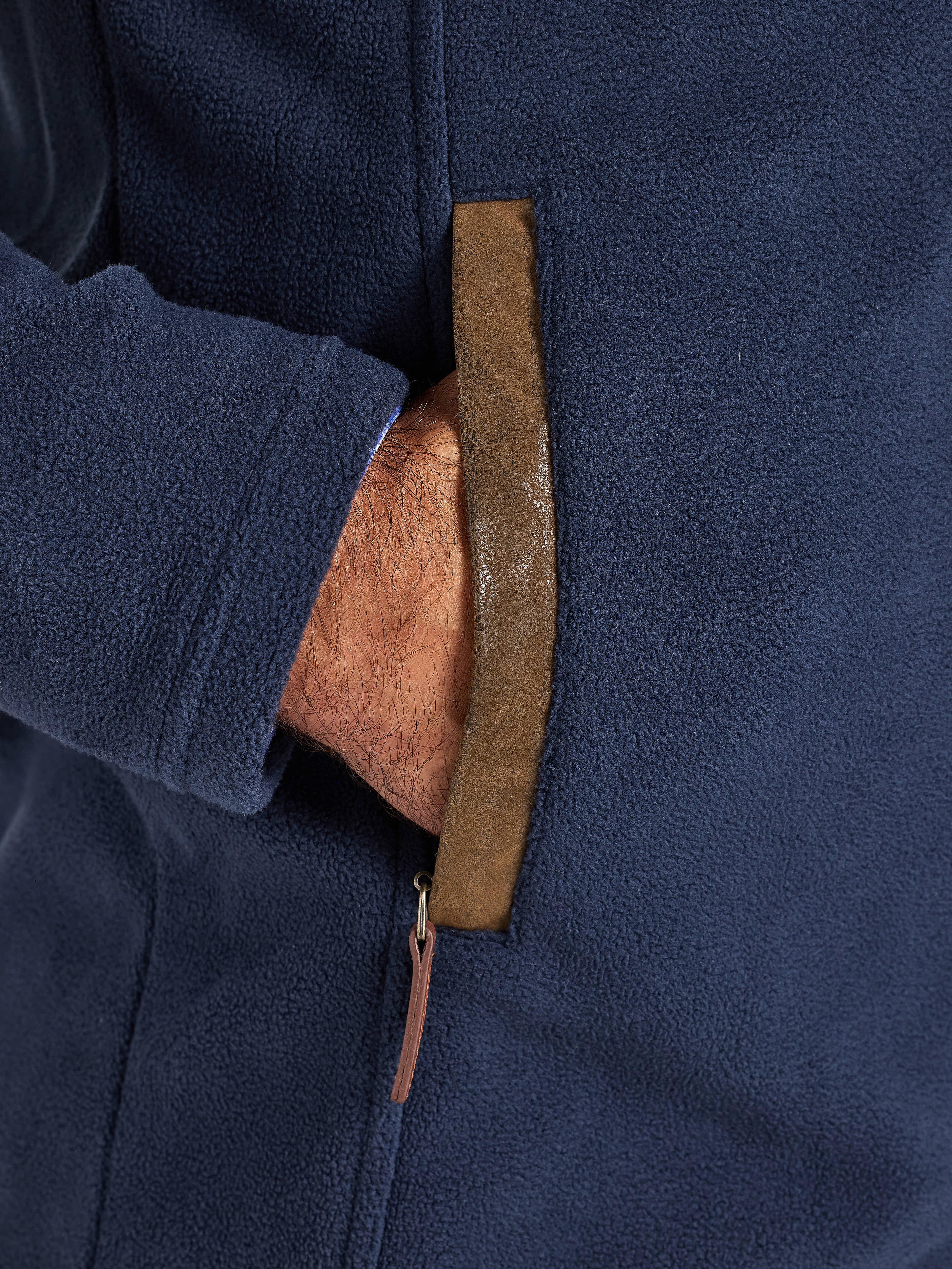 Close-up of a navy blue jacket with a brown leather strap and zipper.