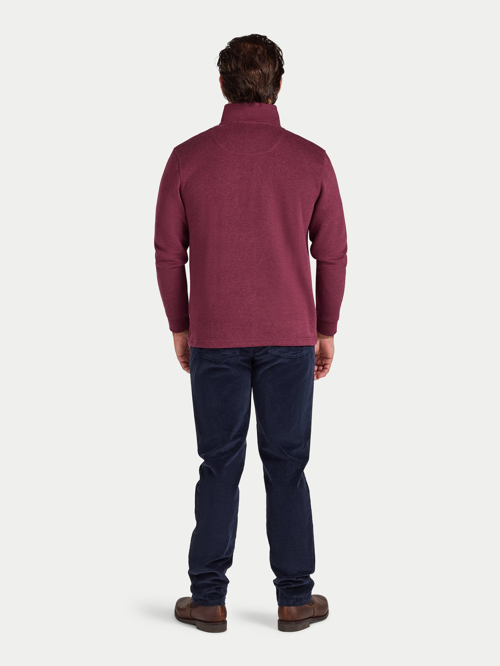 Man wearing a maroon sweater and dark blue jeans on a white background