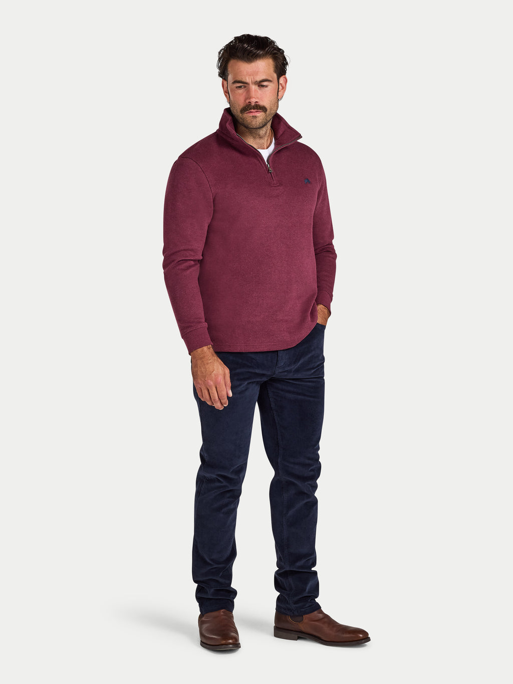 Man wearing a maroon sweater and dark jeans on a white background