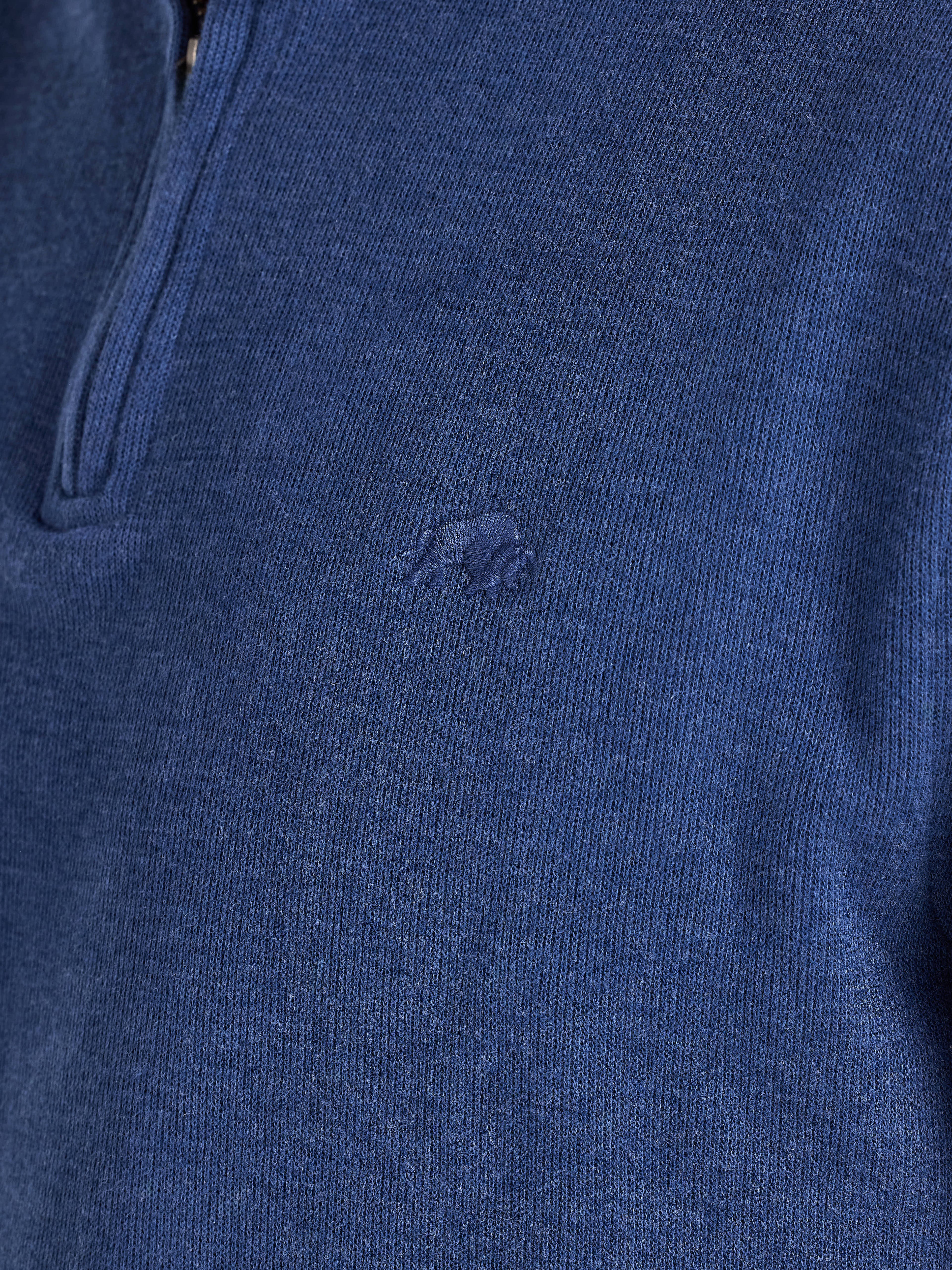 Close-up of a blue sweater with a brand logo on a dark background
