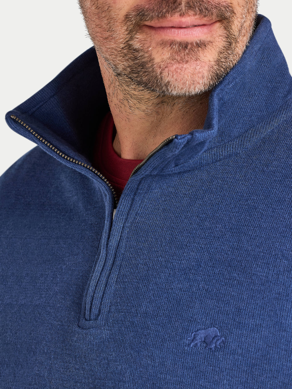 Close-up of a person wearing a blue half-zip sweatshirt with a brand logo on a white background