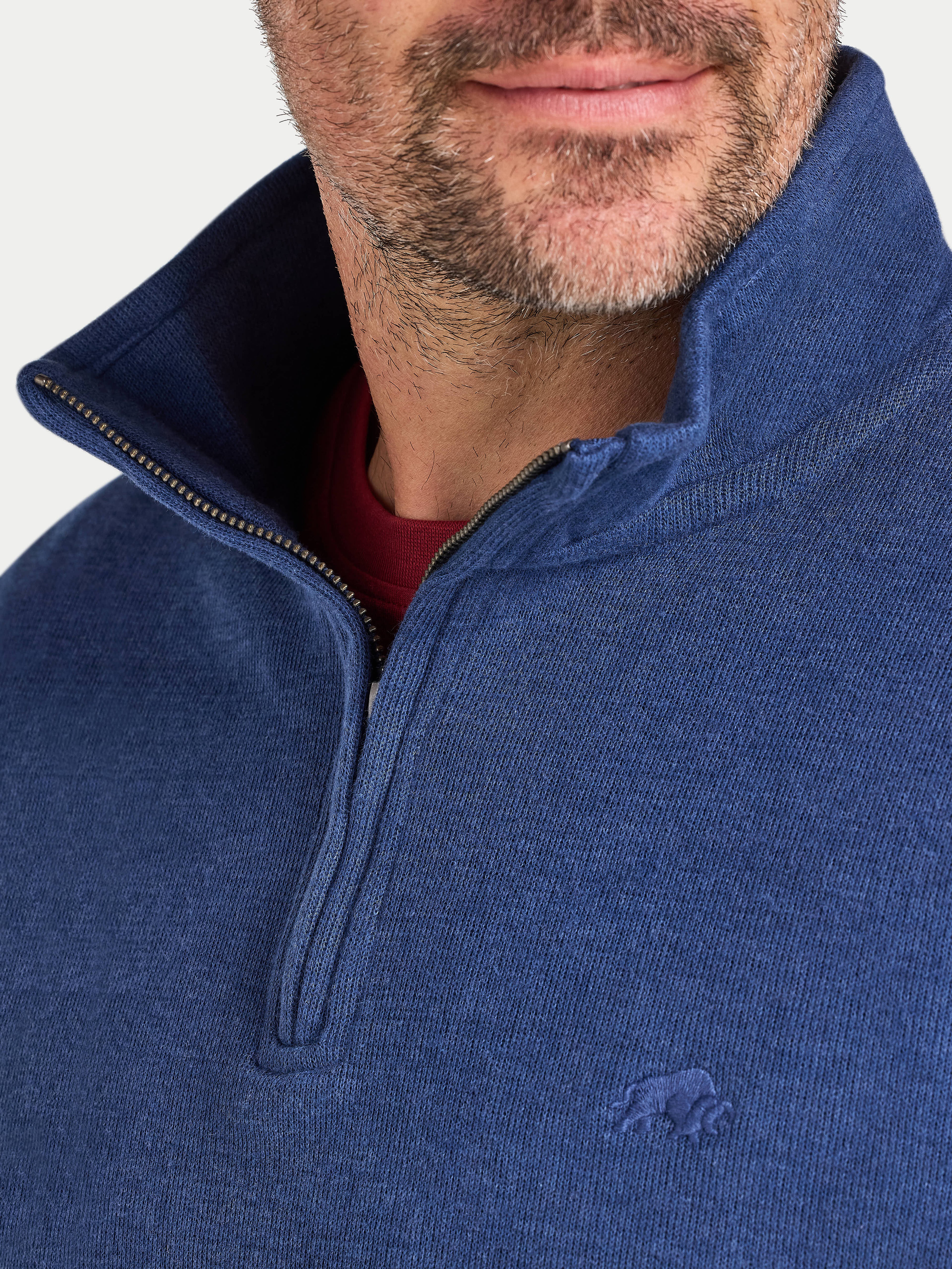 Close-up of a person wearing a blue half-zip sweatshirt with a brand logo on a white background