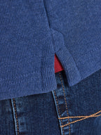 Close-up of a blue sweater with a red lining peeking out and blue jeans.