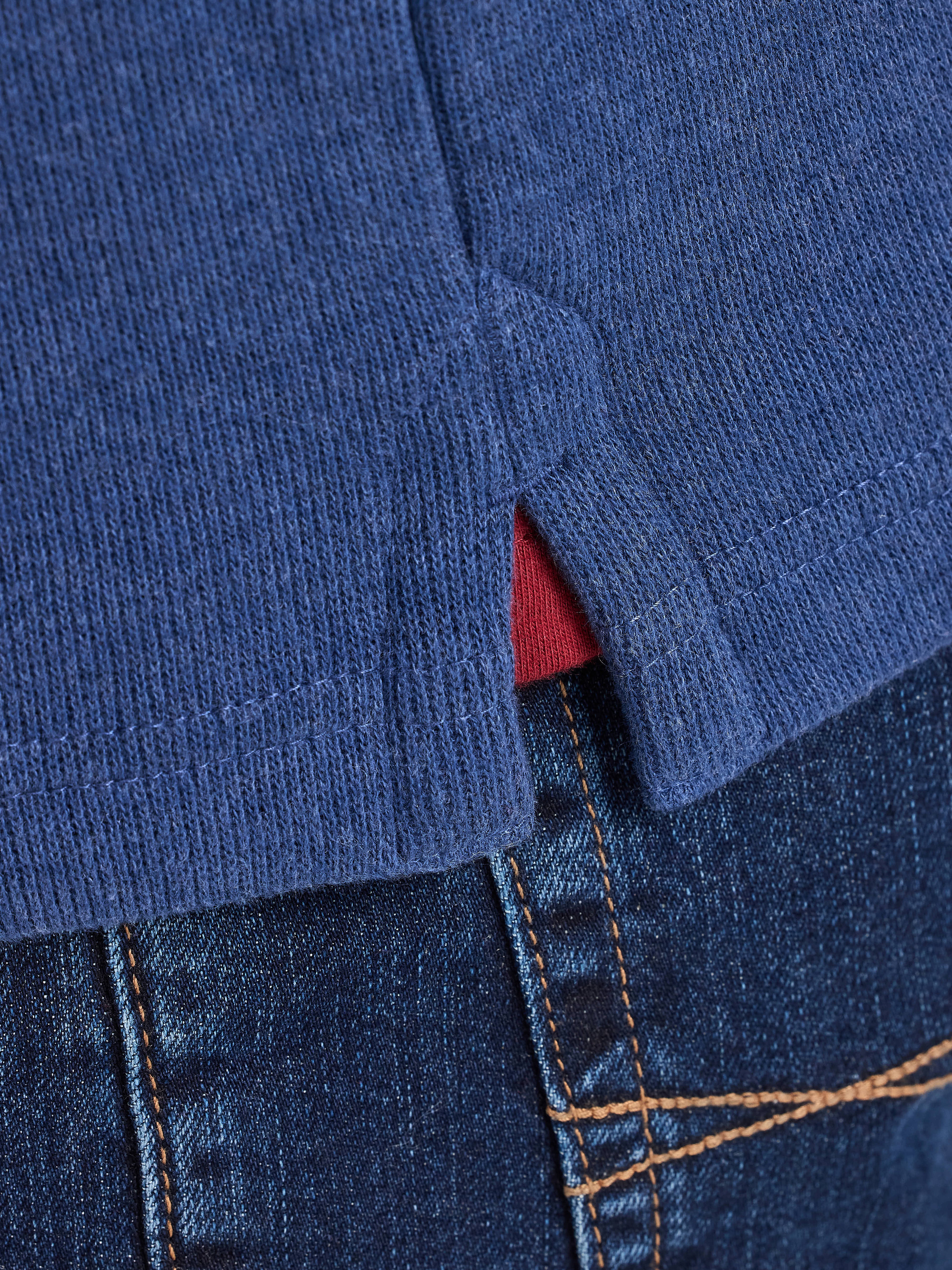 Close-up of a blue sweater with a red lining peeking out and blue jeans.