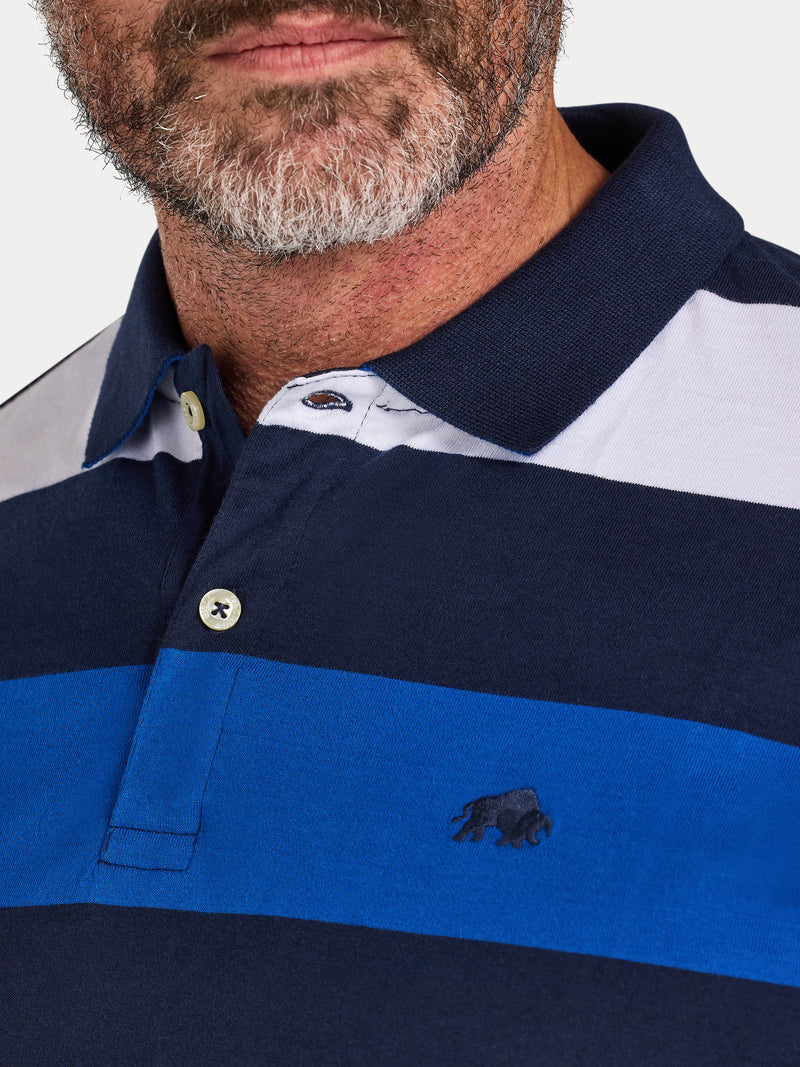 Close-up of a man wearing a navy and blue striped polo shirt with a Raging Bull logo.