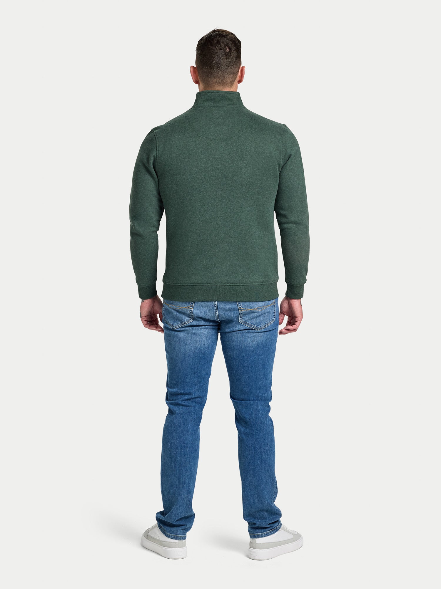 Man wearing a green sweater and blue jeans on a white background