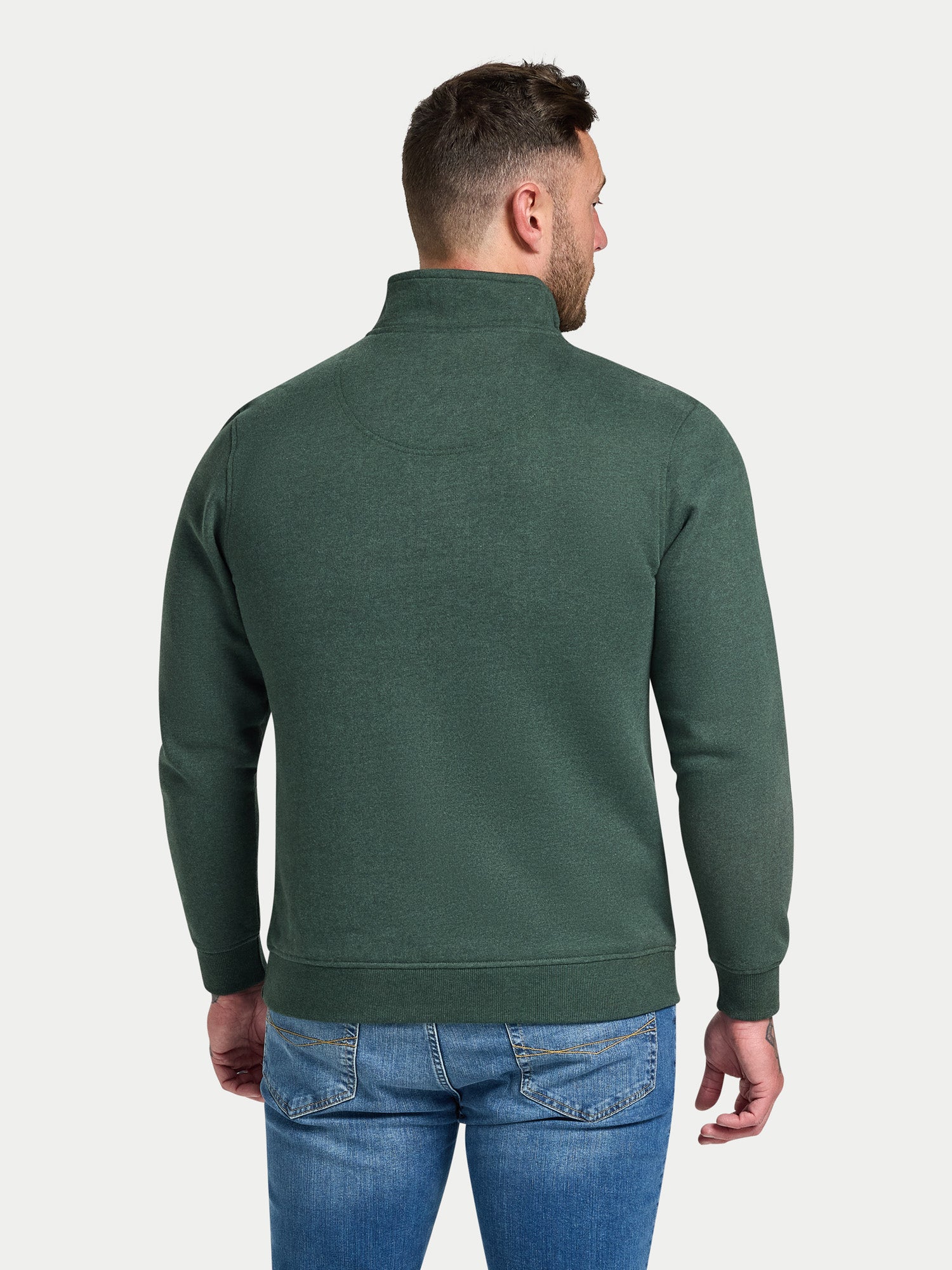 Man wearing a green half-zip sweatshirt and blue jeans on a white background