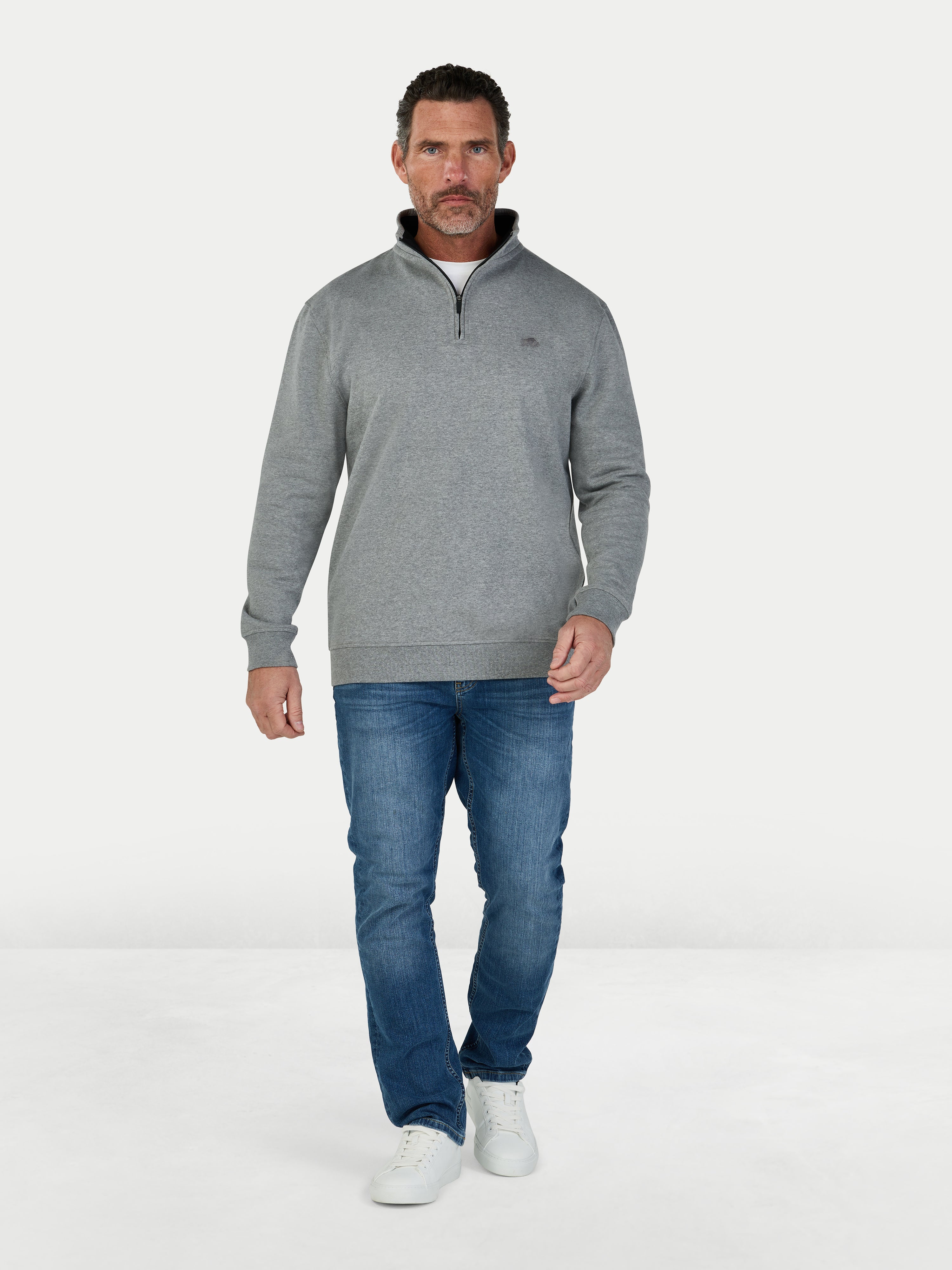 Man wearing a gray sweater and blue jeans on a white background