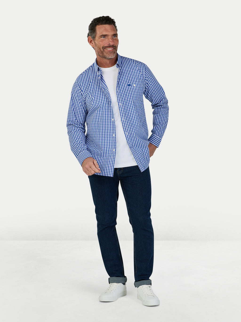 Man wearing a blue checkered shirt, white t-shirt, and dark jeans on a white background