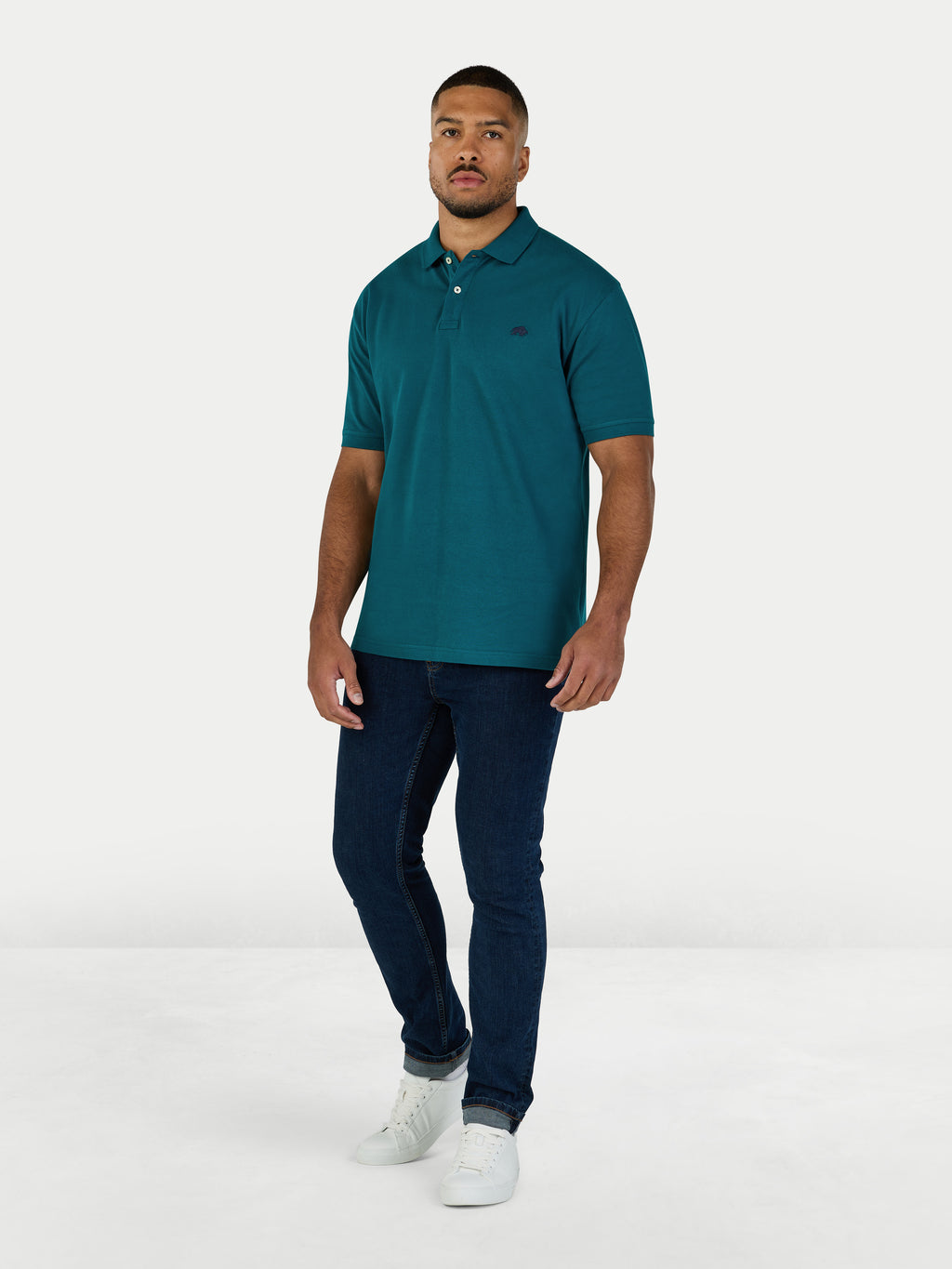 Man wearing a teal polo shirt and dark jeans on a white background