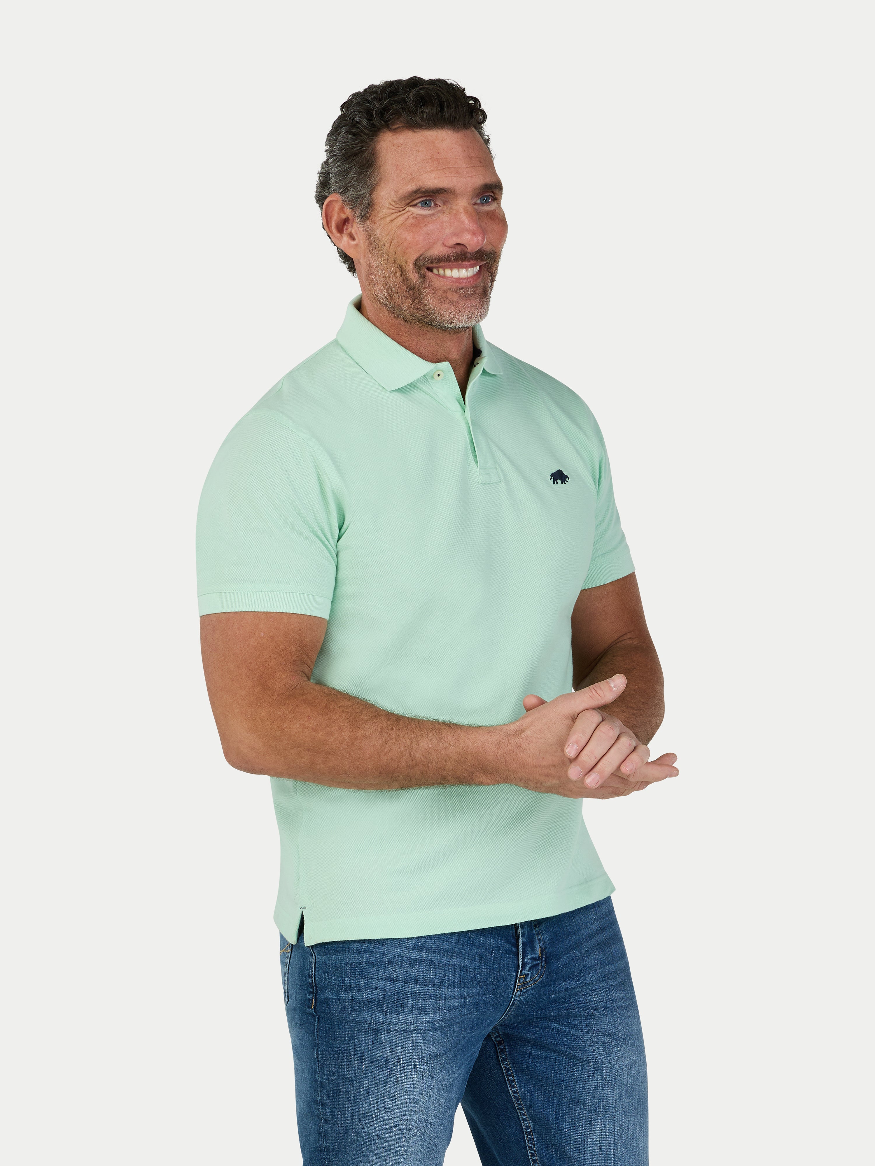 Man wearing a light green polo shirt and blue jeans on a white background
