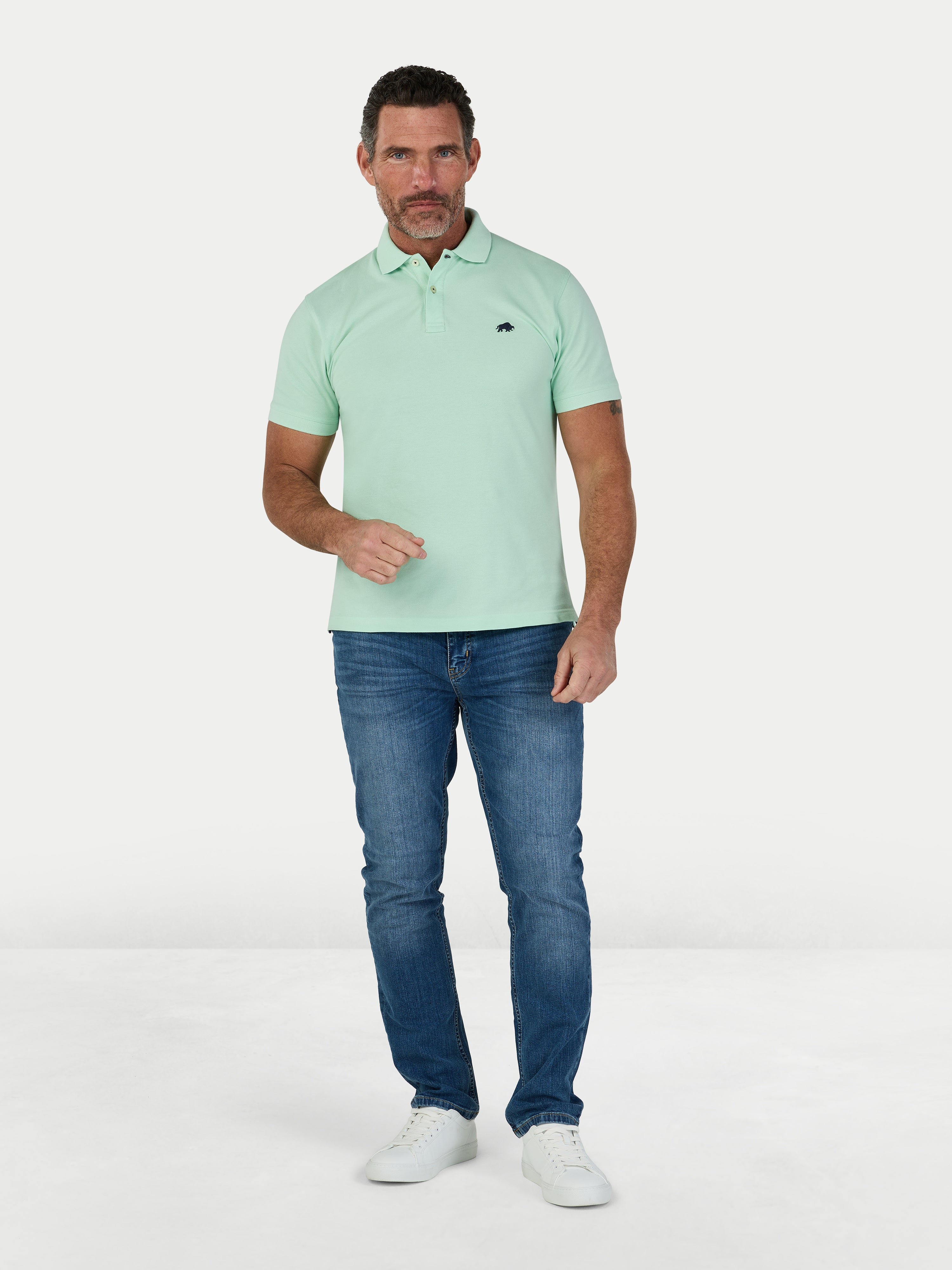 Man wearing a light green polo shirt and blue jeans on a white background