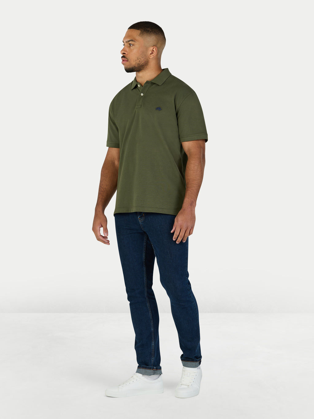 Man wearing a green polo shirt and dark jeans on a white background
