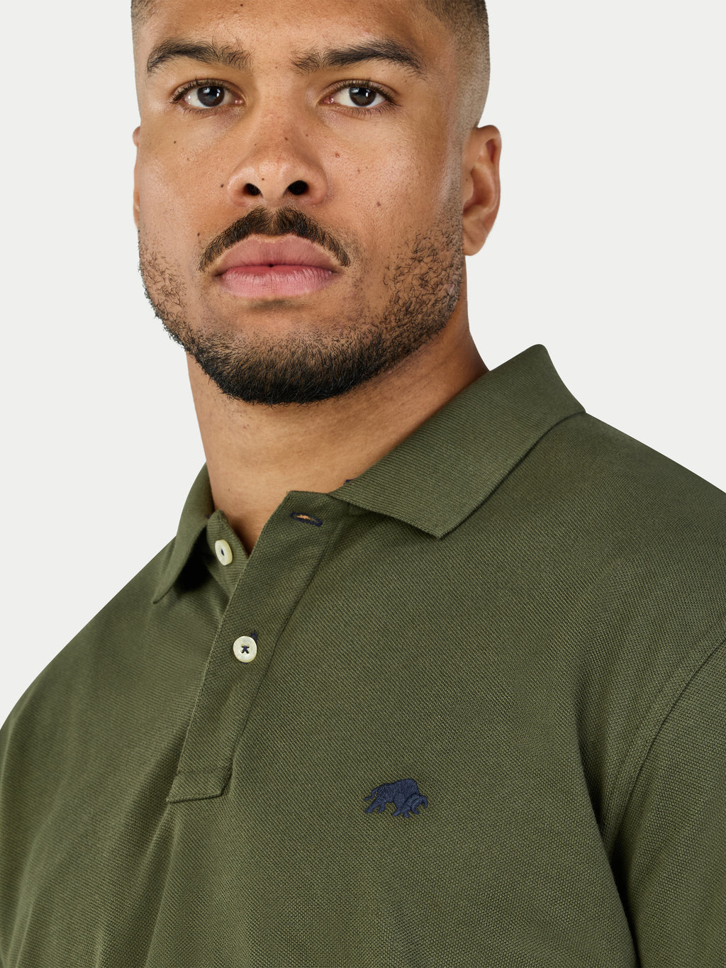Man wearing a green polo shirt with a logo on a white background