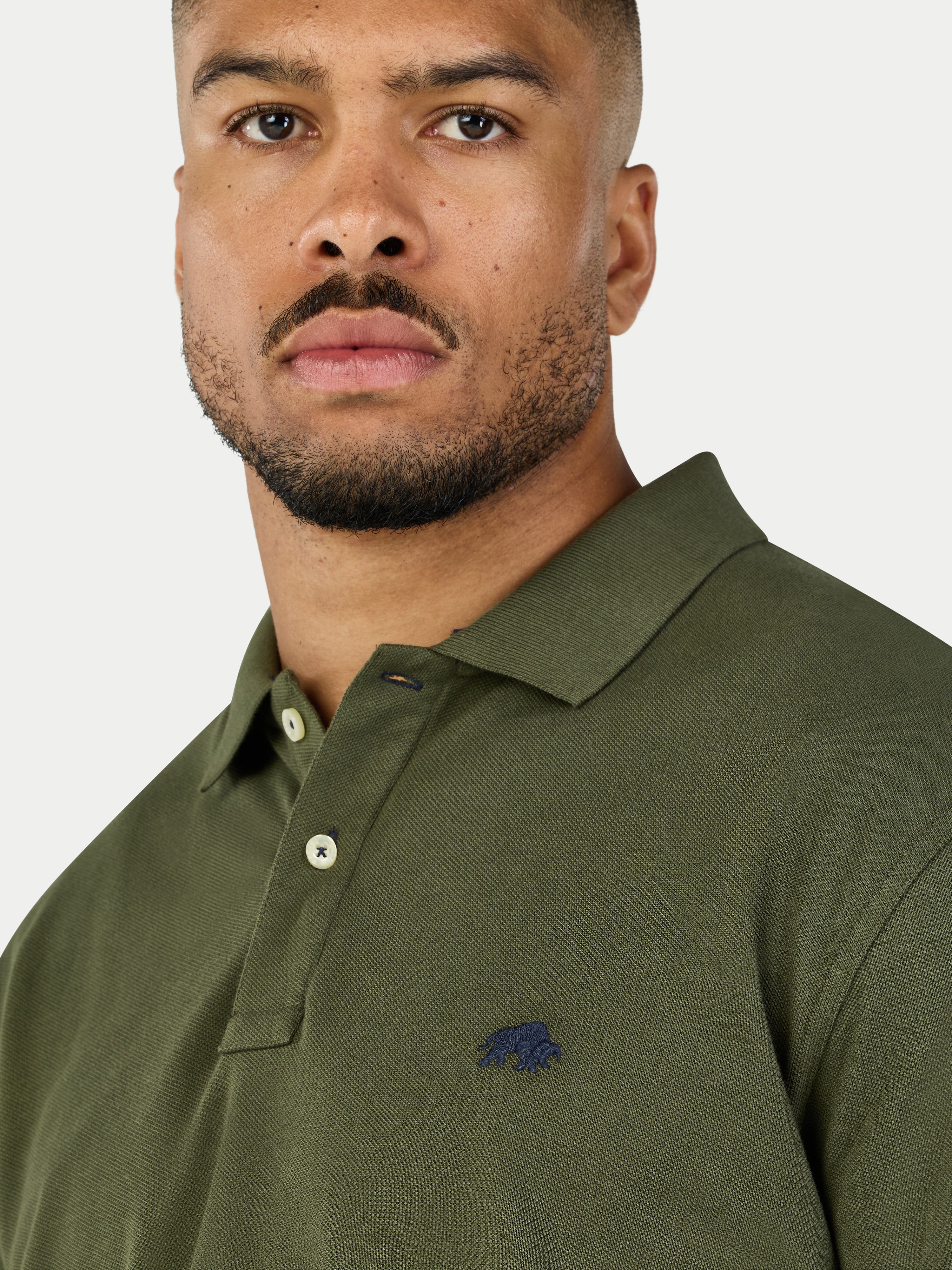 Man wearing a green polo shirt with a logo on a white background