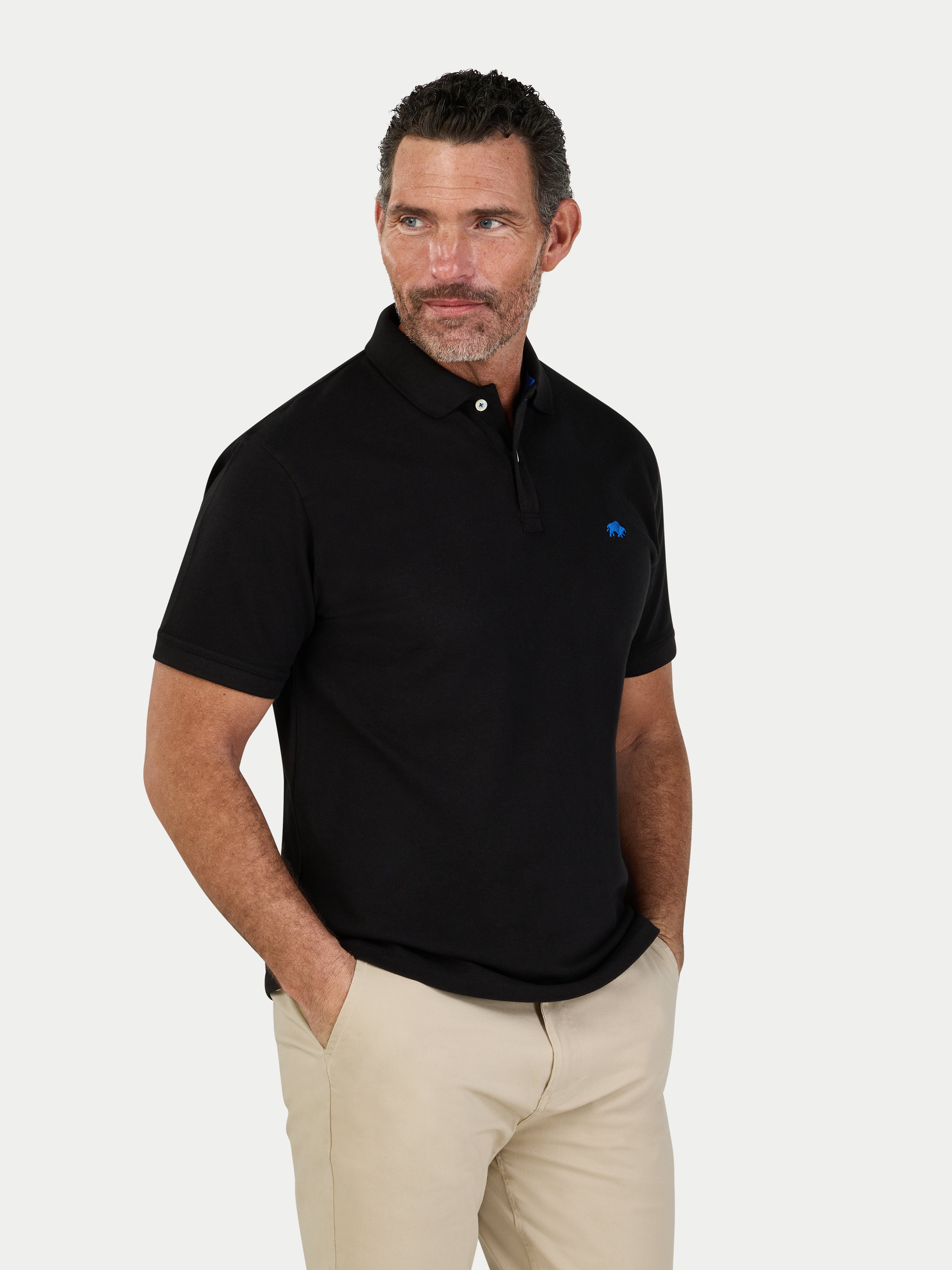 Man wearing a black polo shirt with a logo on a white background.