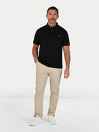 Man wearing a black polo shirt with a logo and beige pants on a white background.