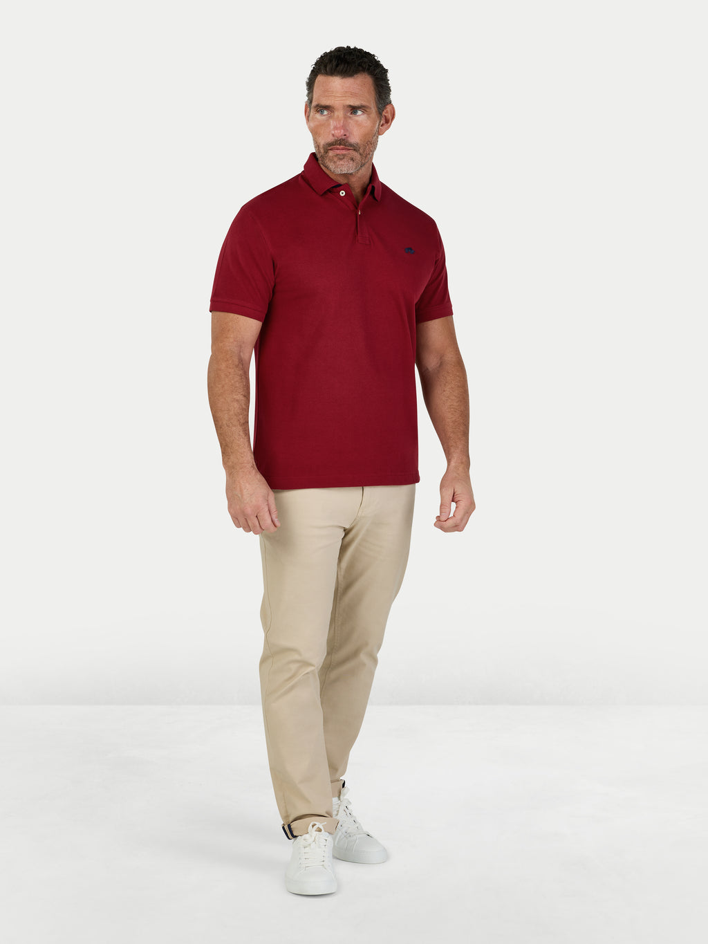 Man wearing a red polo shirt and beige pants on a white background.