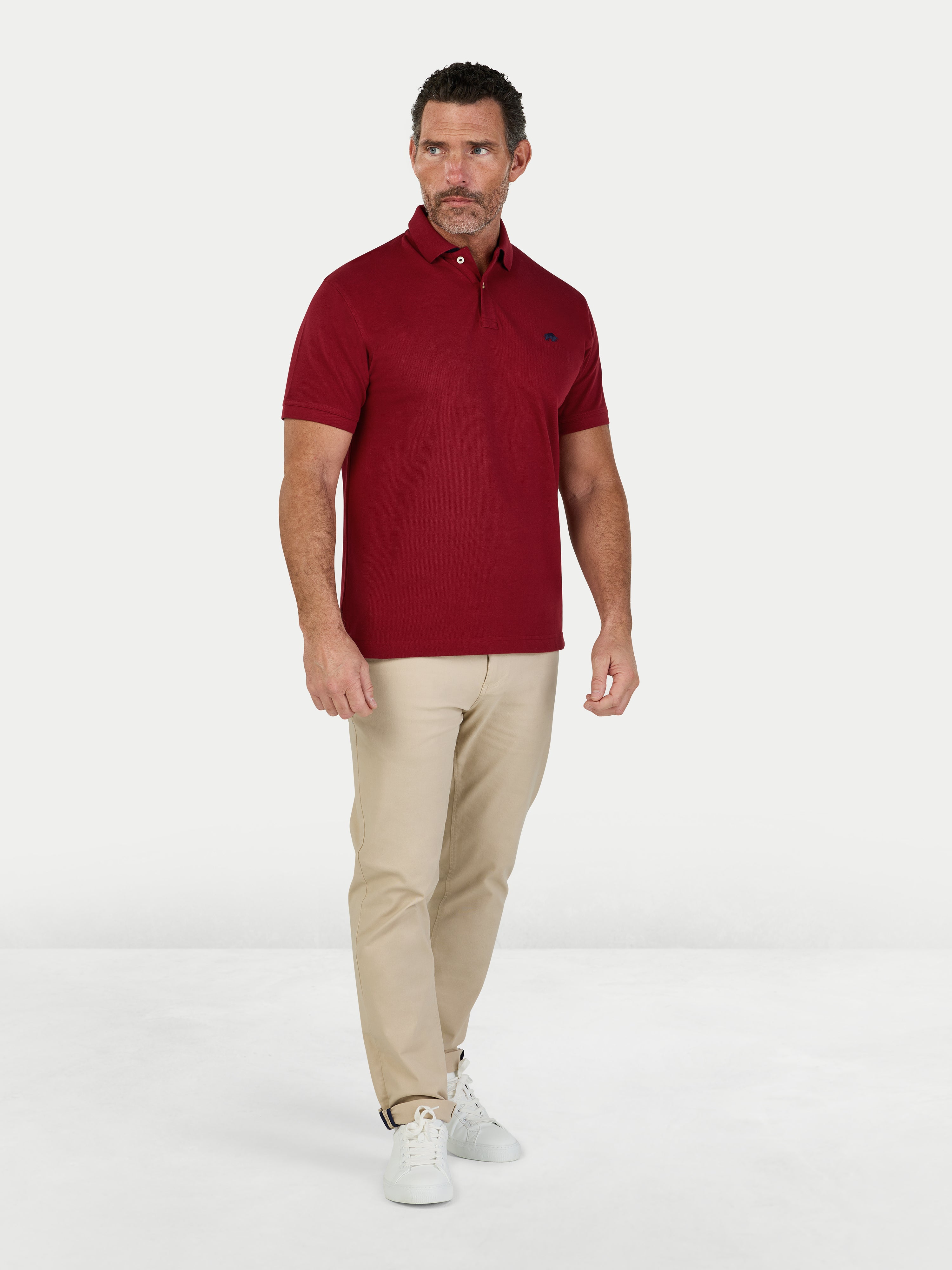 Man wearing a red polo shirt and beige pants on a white background.