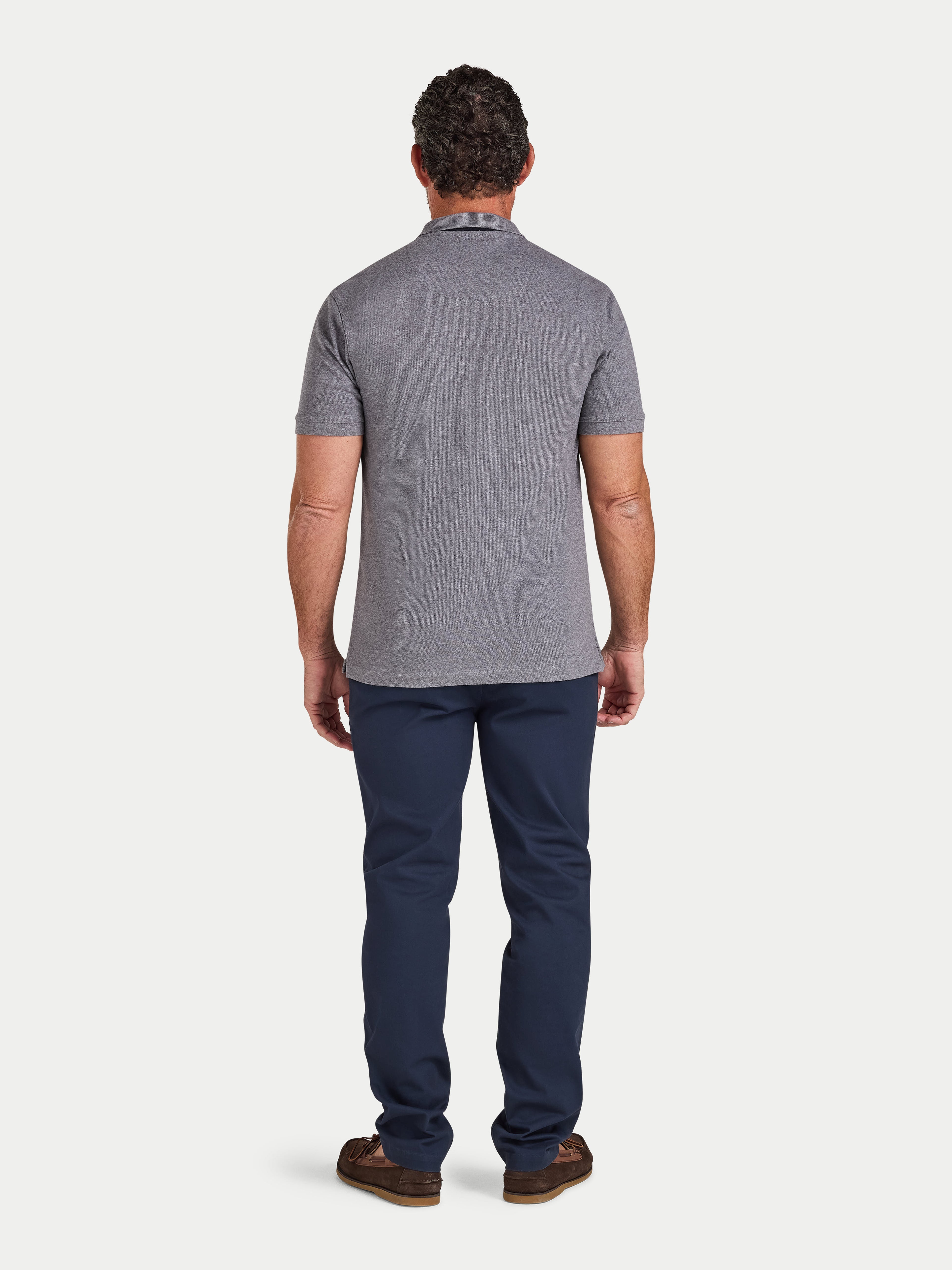 Man wearing a gray polo shirt and navy pants on a white background