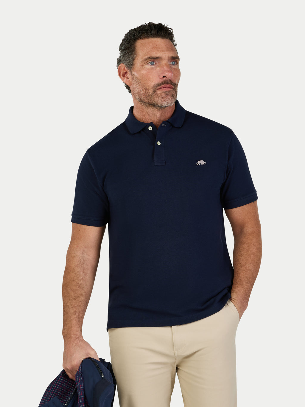 Man wearing a navy polo shirt with a logo, holding a blue bag on a light gray background