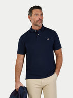 Man wearing a navy polo shirt with a logo, holding a blue bag on a light gray background