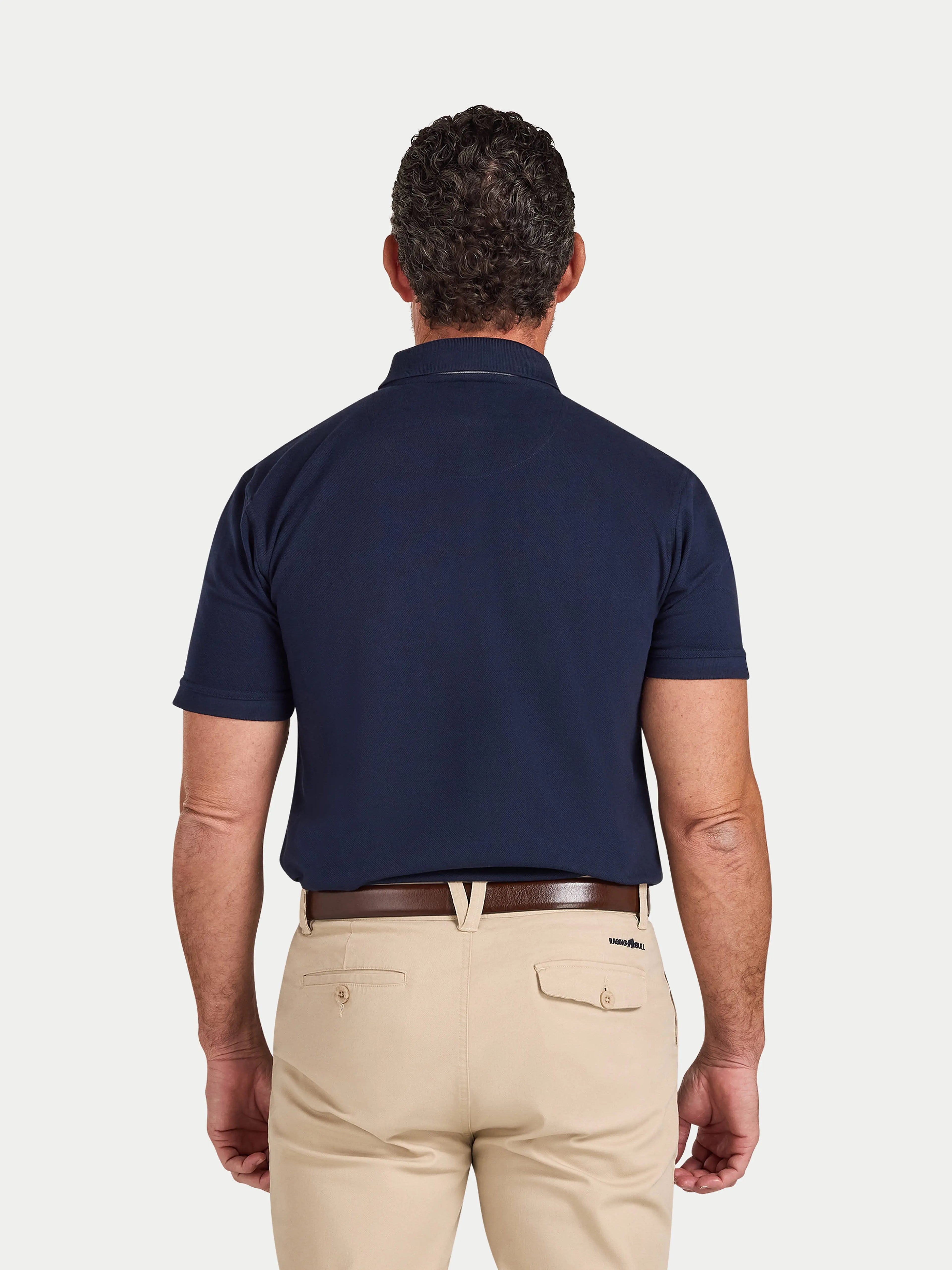 Man wearing a navy polo shirt and beige pants on a light gray background