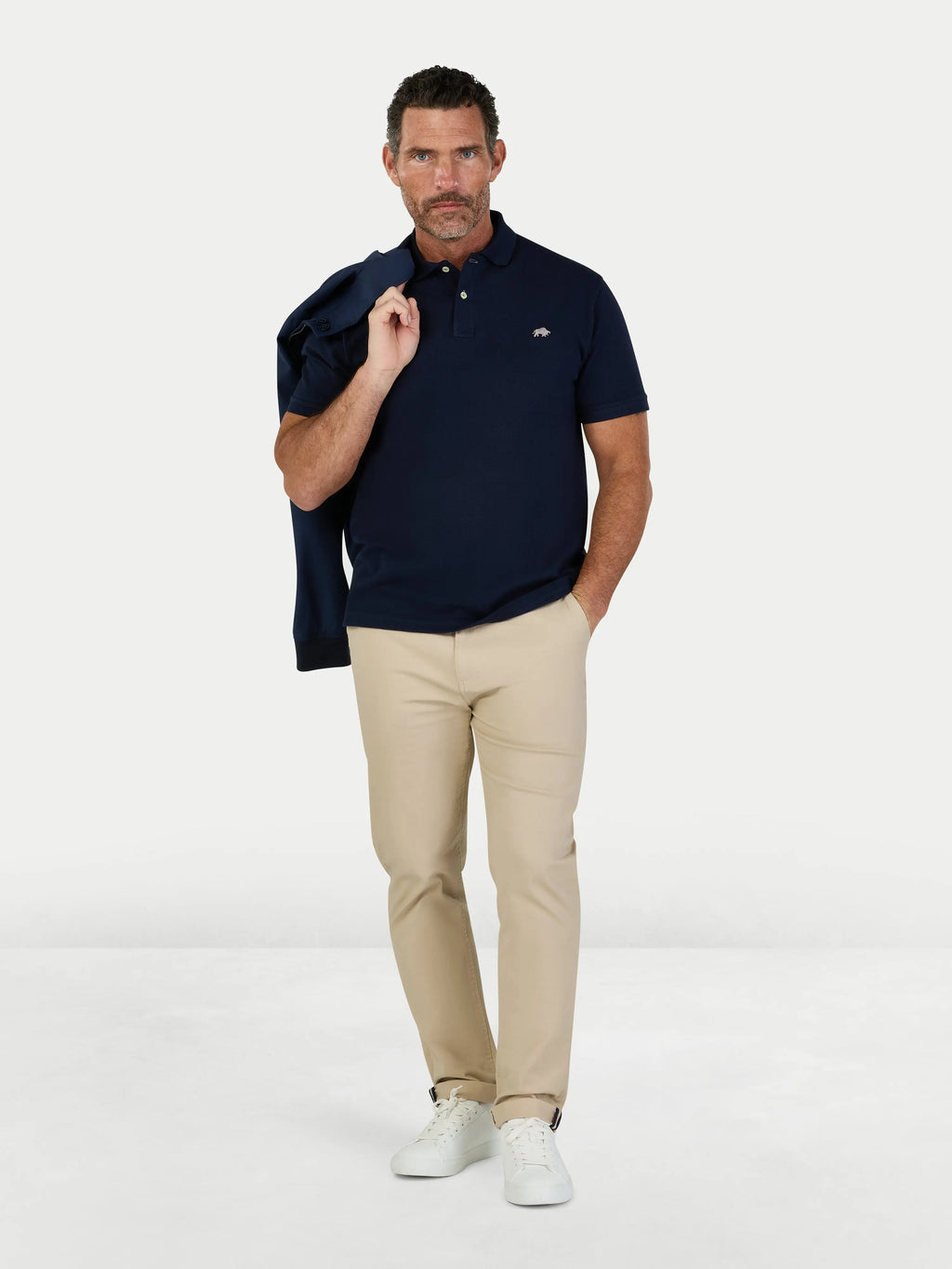 Man wearing a navy polo shirt and beige pants on a white background
