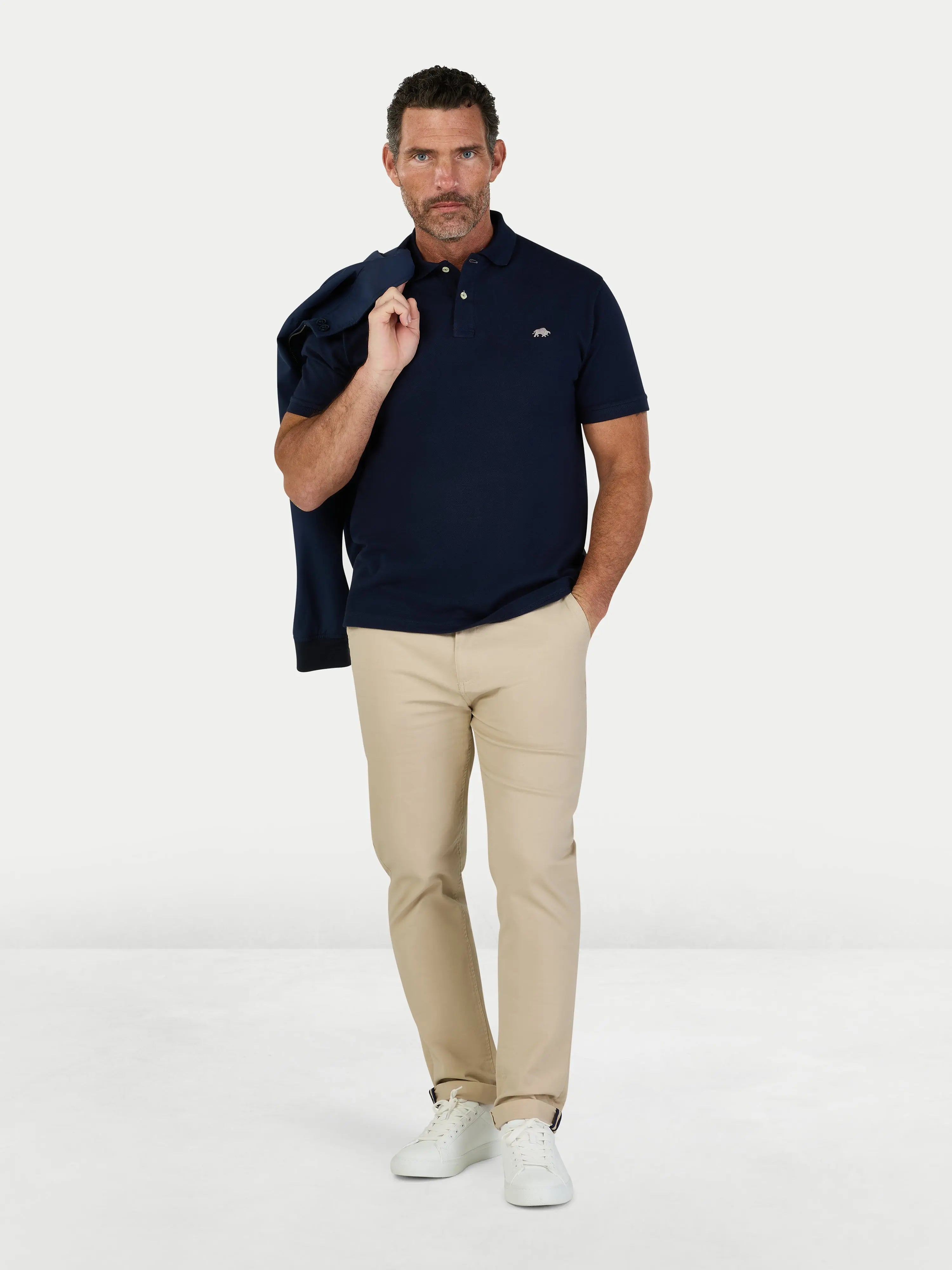 Man wearing a navy polo shirt and beige pants on a white background