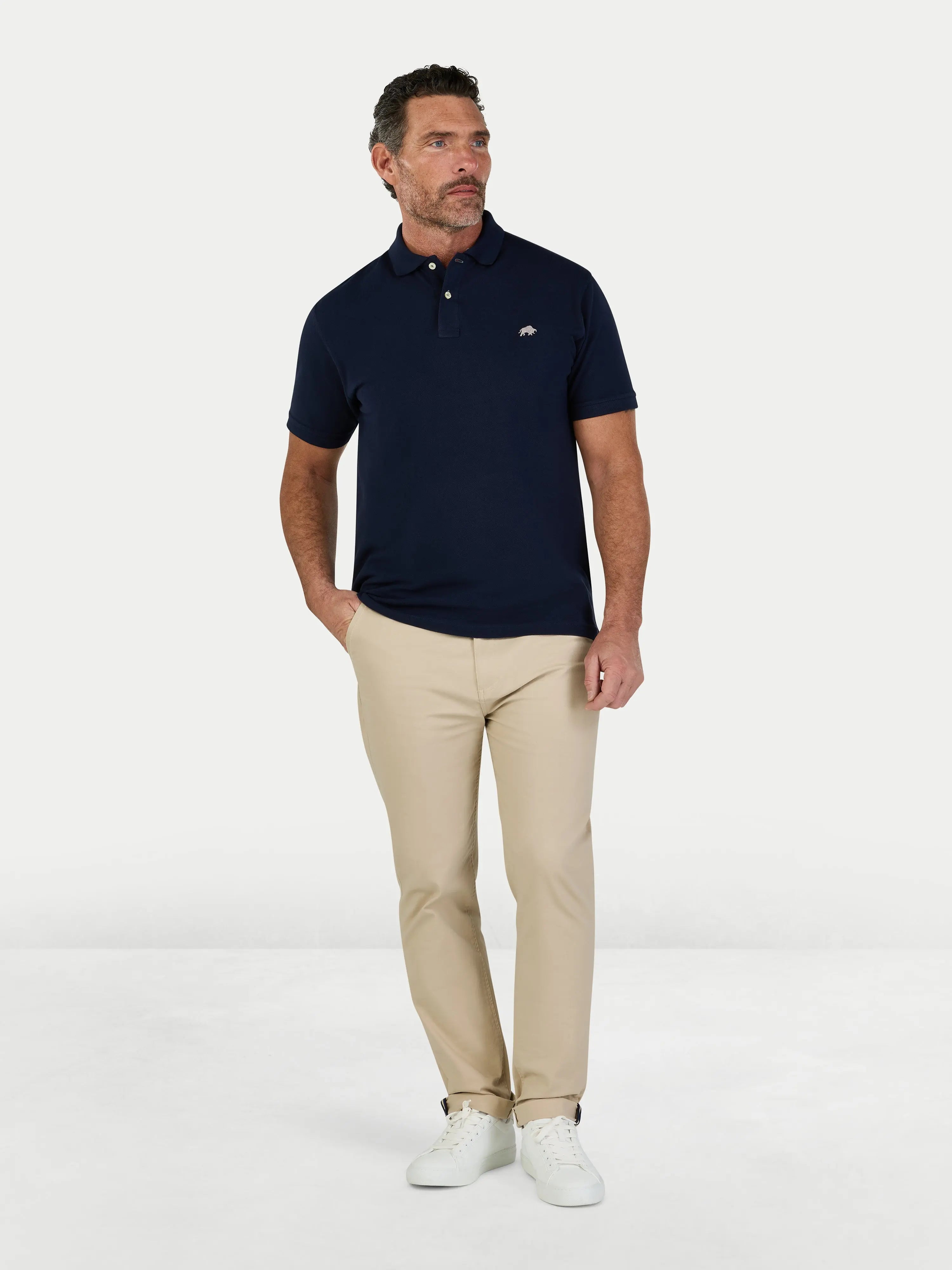Man wearing a navy polo shirt and beige pants on a white background