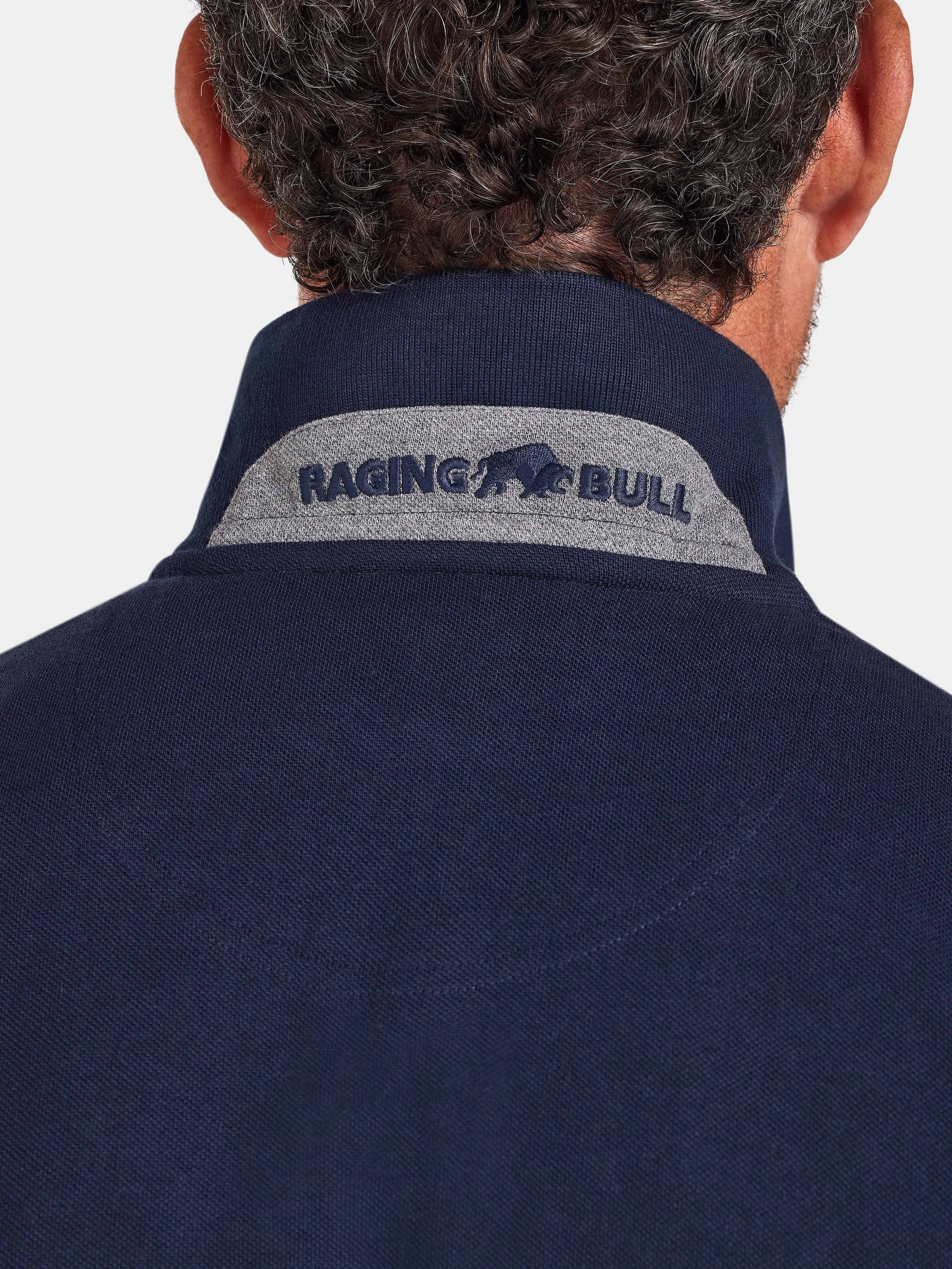 Navy blue polo shirt with 'Raging Bull' logo on the collar against a light gray background