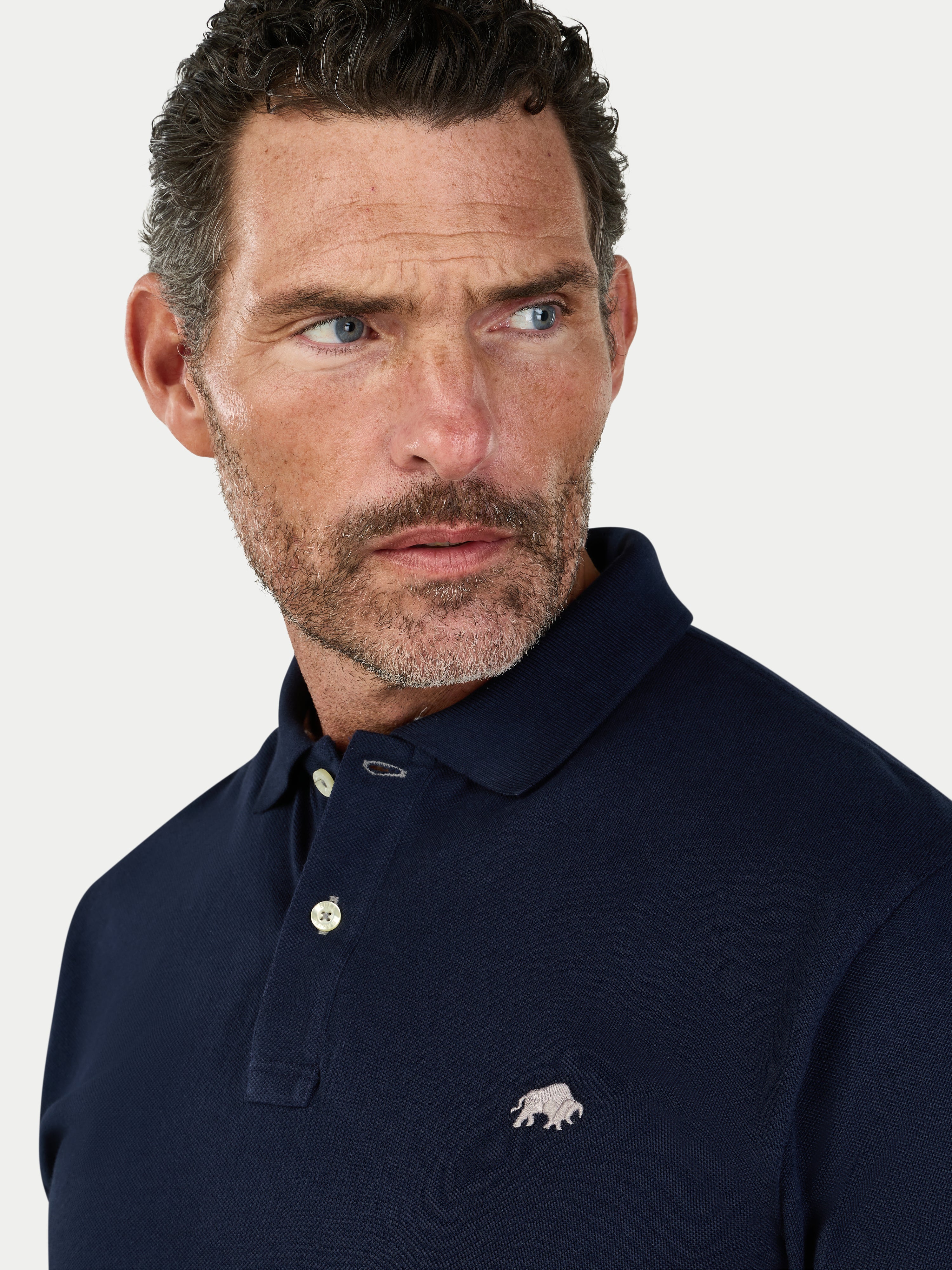 Man wearing a navy polo shirt with a logo on a light gray background