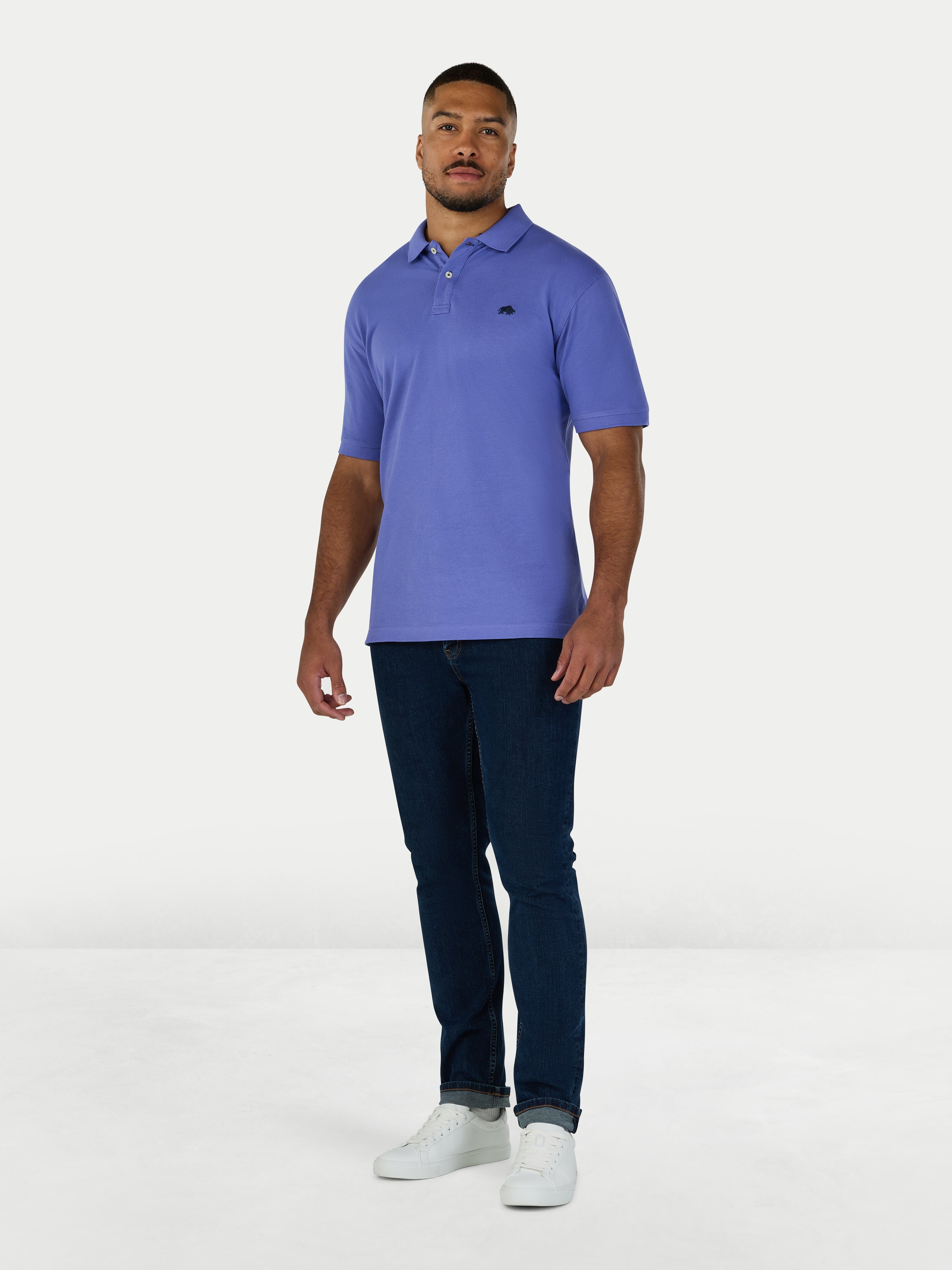Man wearing a purple polo shirt and dark jeans on a white background