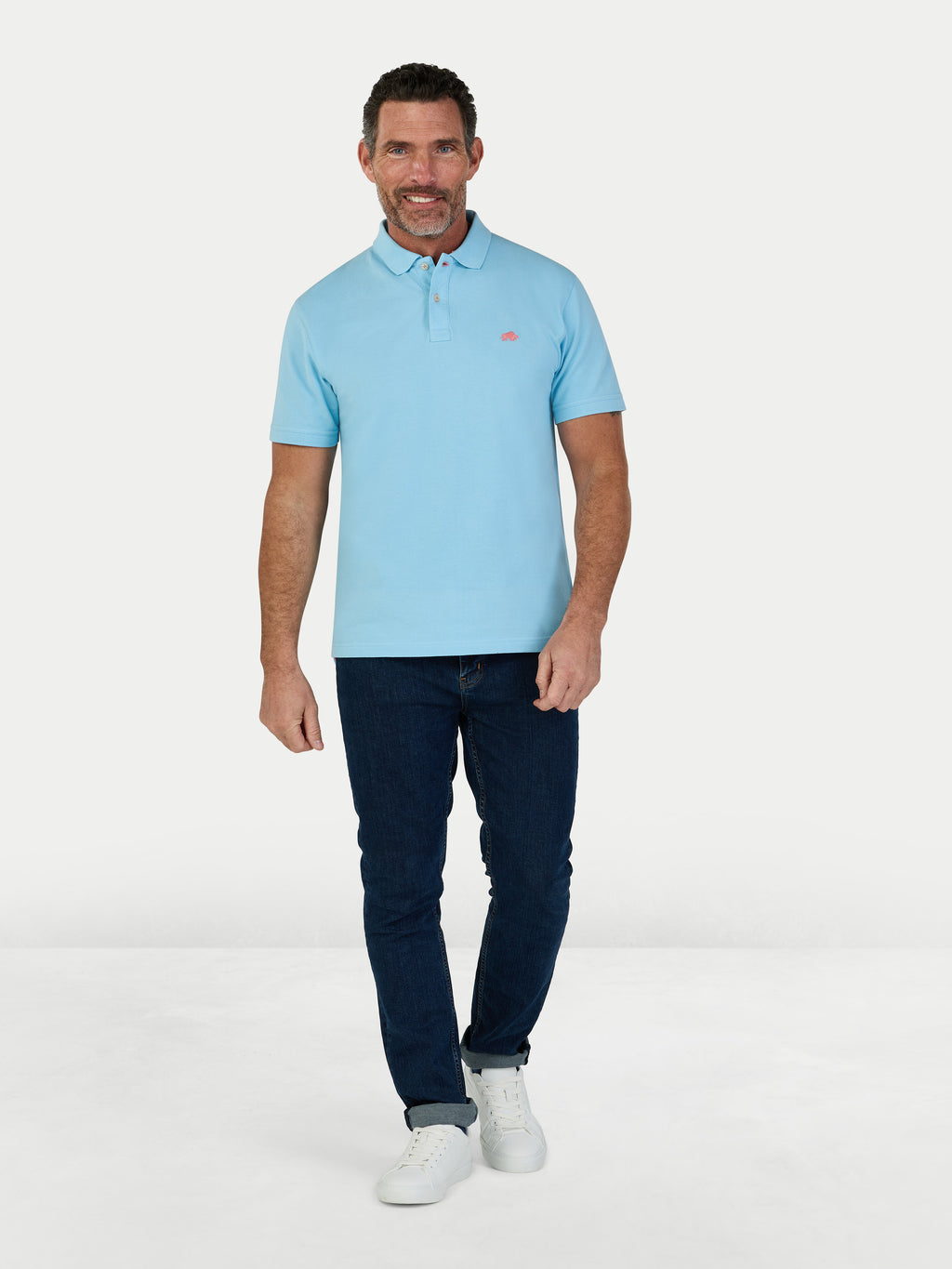 Man wearing a light blue polo shirt and dark jeans on a white background