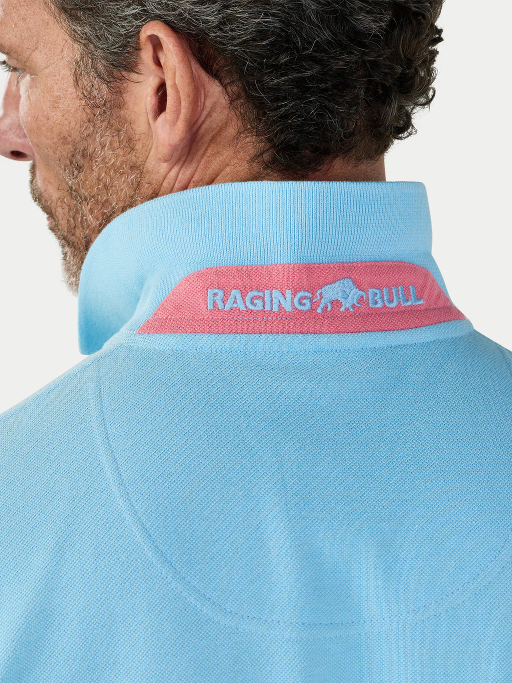 Light blue polo shirt with 'Raging Bull' logo on the collar against a white background