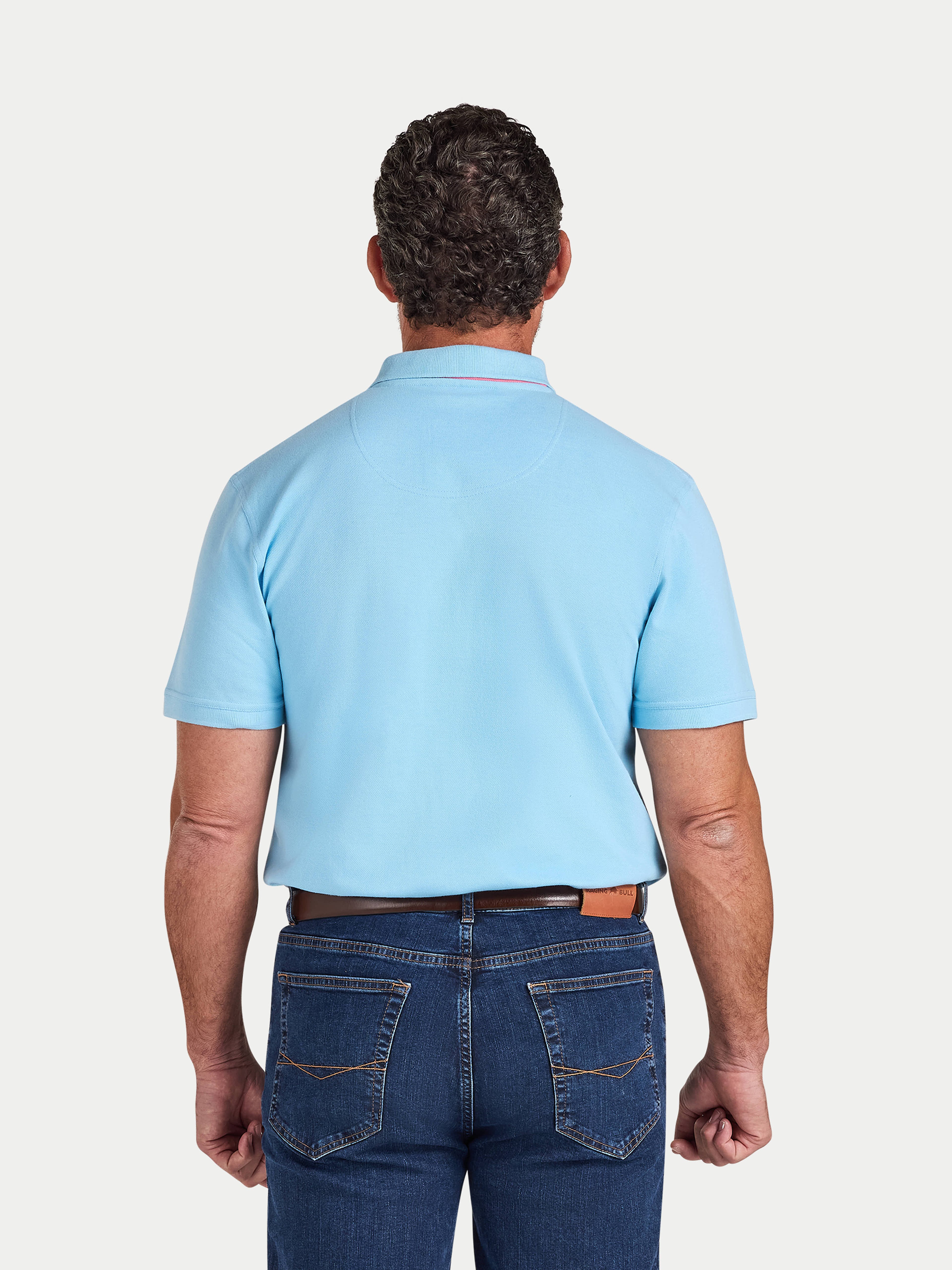 Man wearing a light blue polo shirt and dark blue jeans on a white background