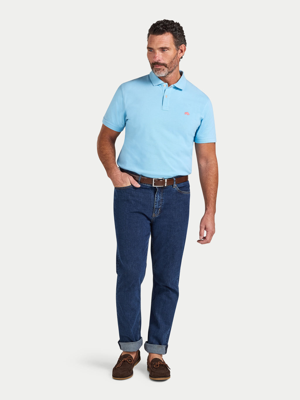 Man wearing a light blue polo shirt and dark blue jeans on a white background
