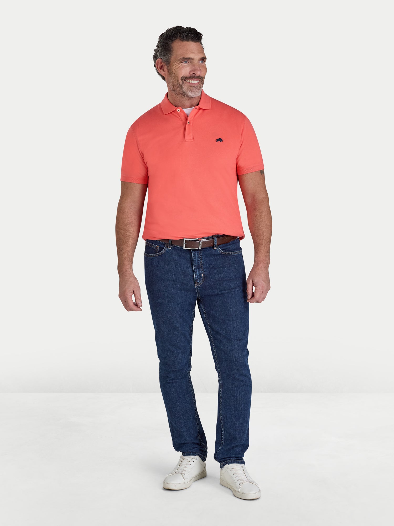 Man wearing a watermelon coloured polo shirt and blue jeans on a white background