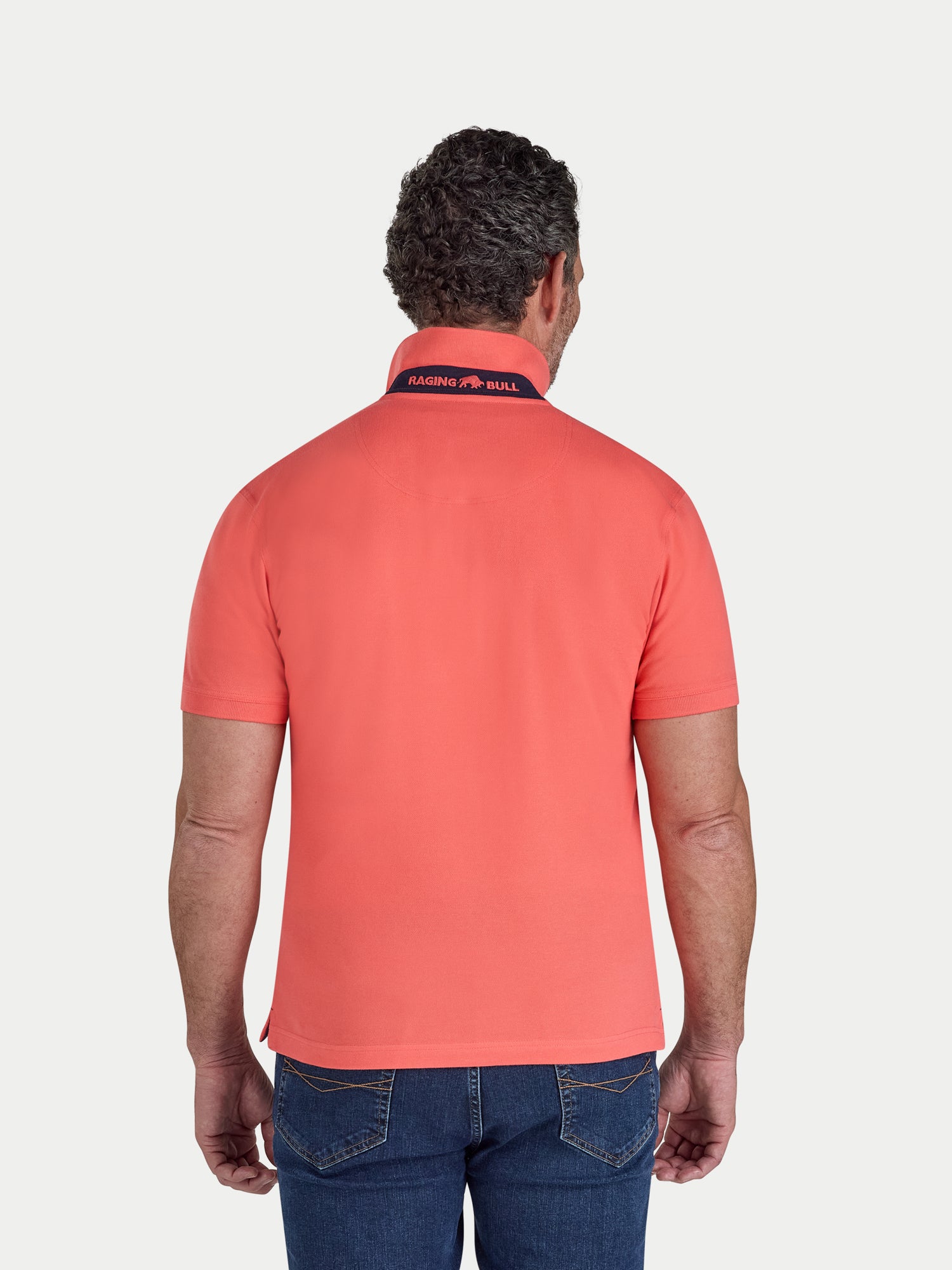 Man wearing a watermelon coloured polo shirt with a visible brand logo on a white background
