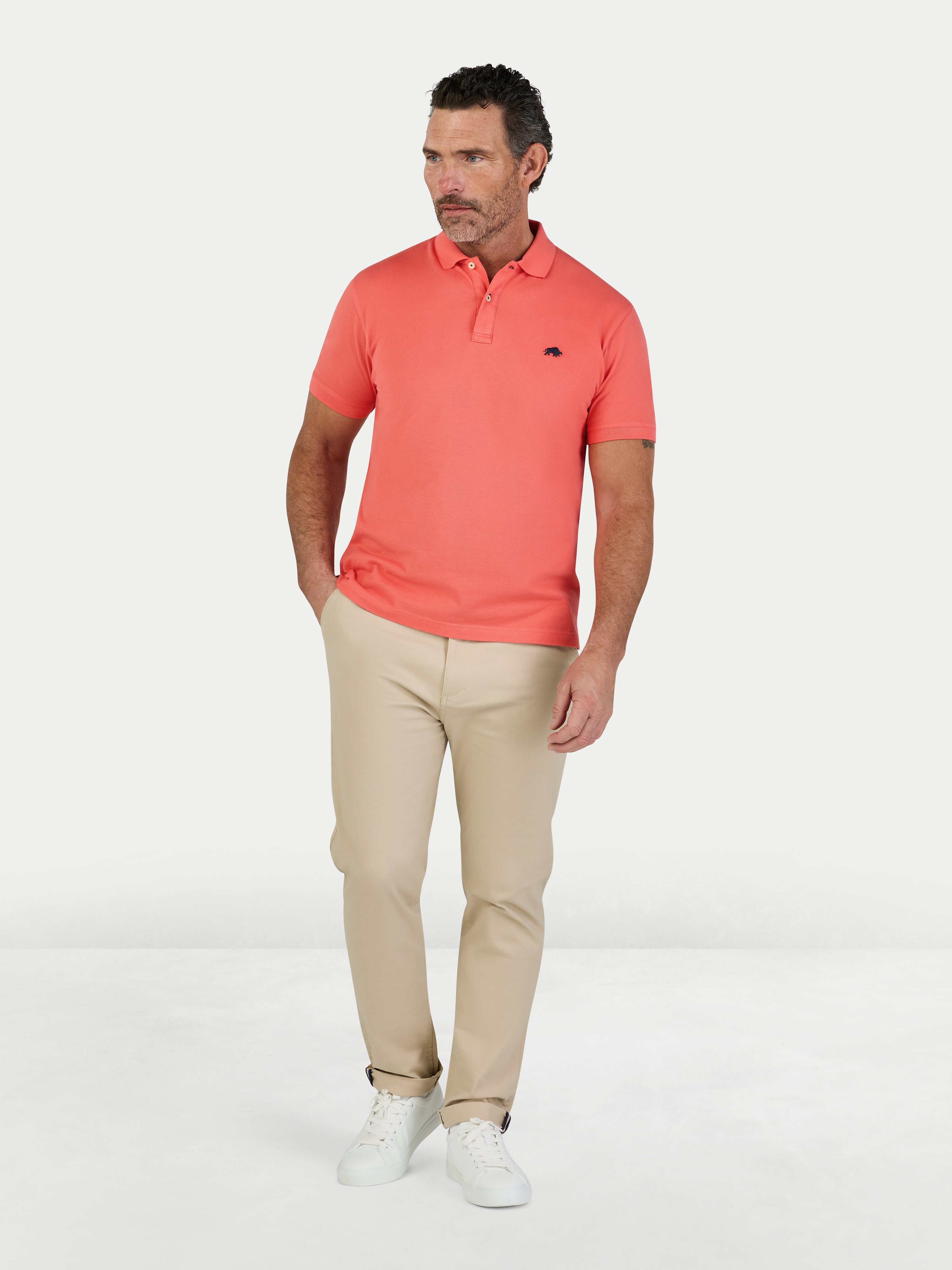 Man wearing a coral polo shirt and beige pants on a white background