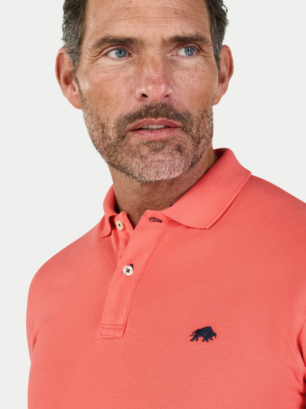 Man wearing a watermelon coloured polo shirt with a logo on a white background