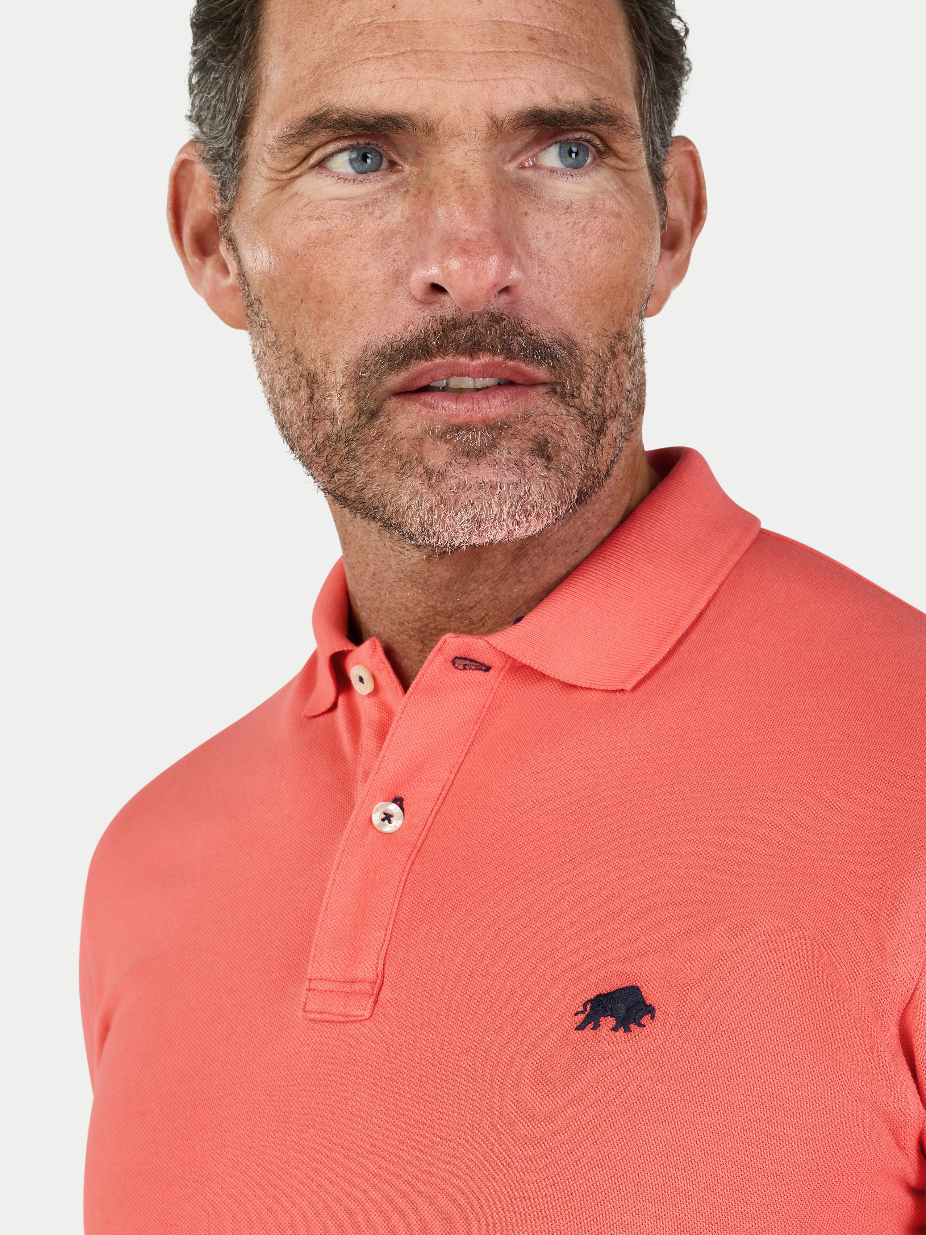 Man wearing a watermelon coloured polo shirt with a logo on a white background