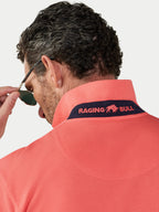 Man wearing a watermelon coloured polo shirt with 'Raging Bull' logo, looking over sunglasses.