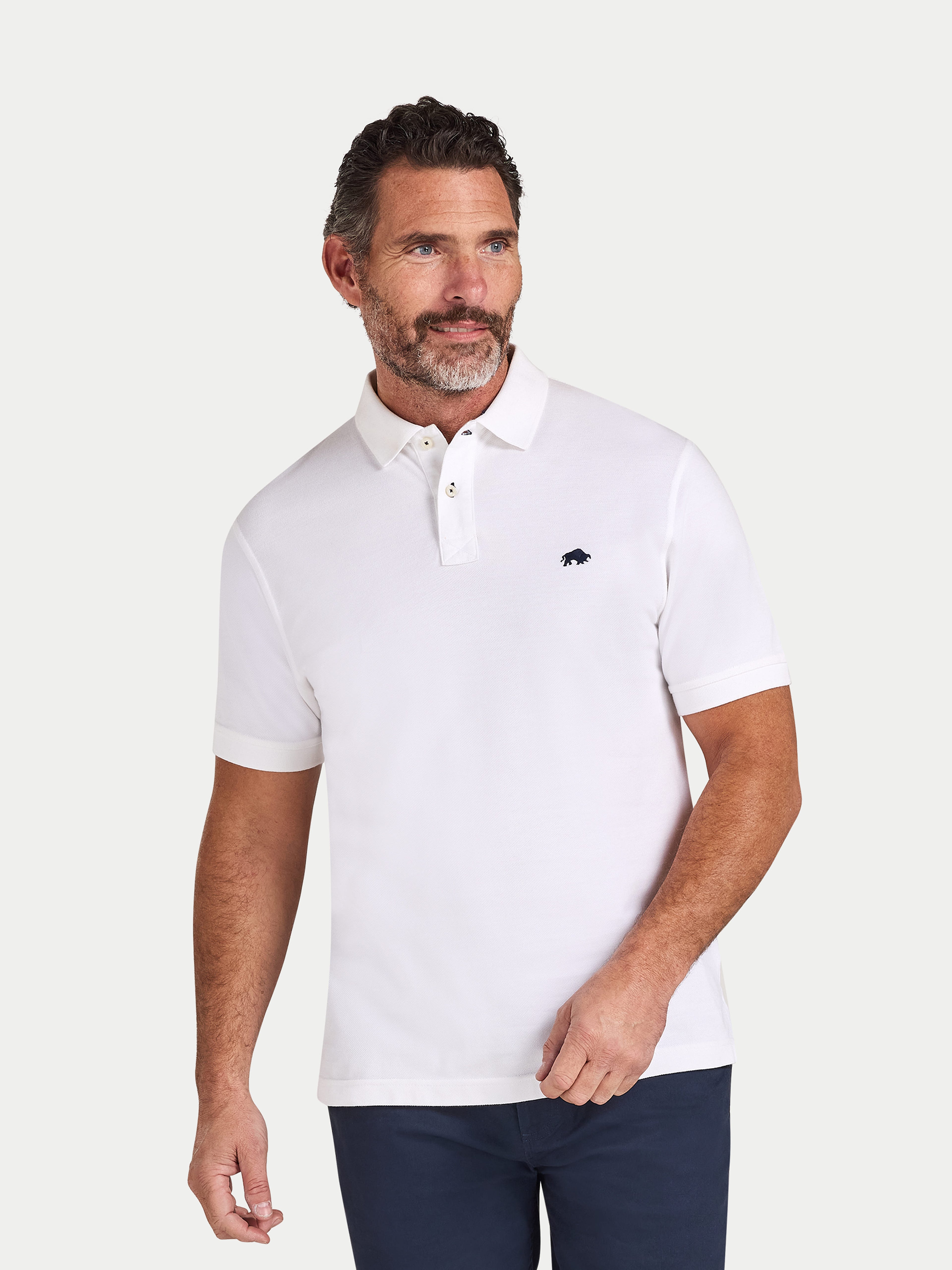 Man wearing a white polo shirt with a small logo on a light gray background