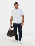 Man wearing a white polo shirt, dark pants, and white shoes, holding a brown bag on a white background