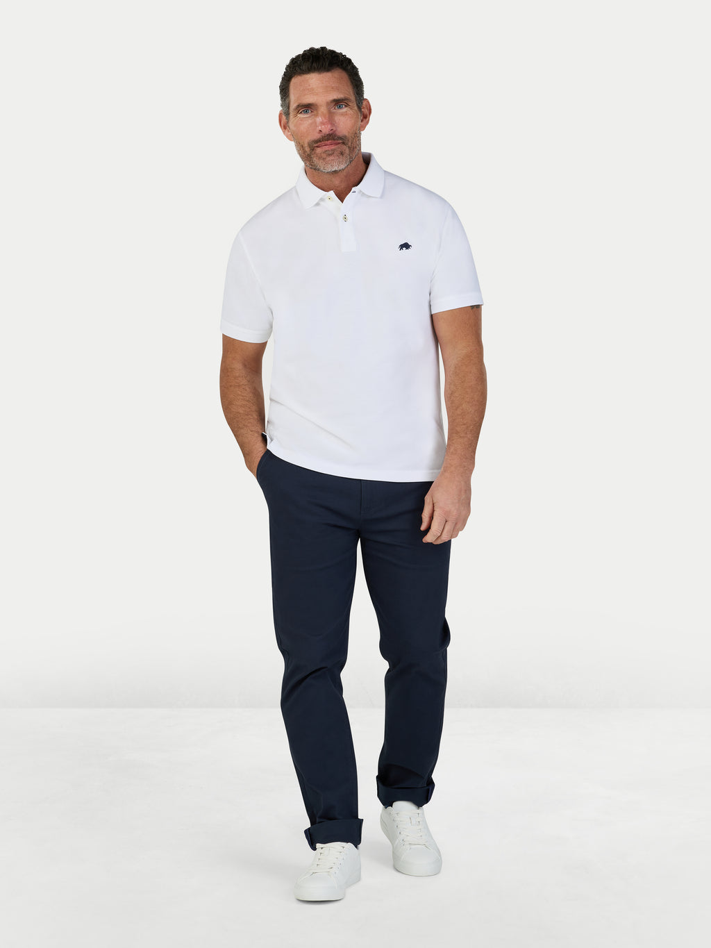 Man wearing a white polo shirt and navy pants on a white background