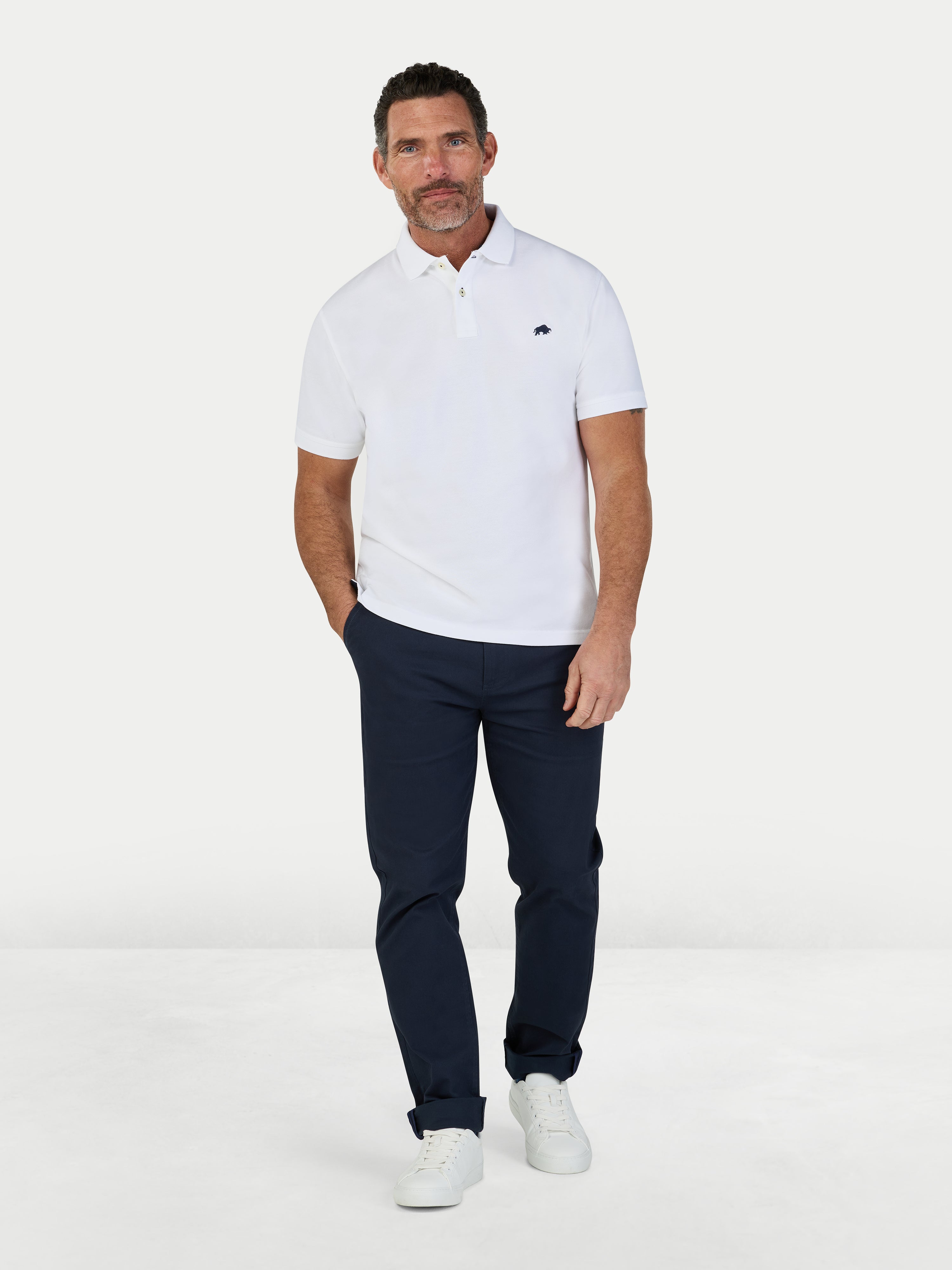 Man wearing a white polo shirt and navy pants on a white background