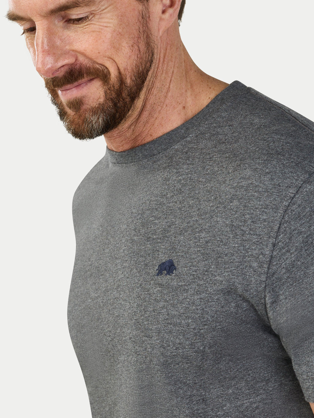 Man wearing a gray t-shirt with a small logo on a light gray background