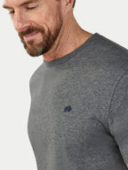 Man wearing a gray t-shirt with a small logo on a light gray background